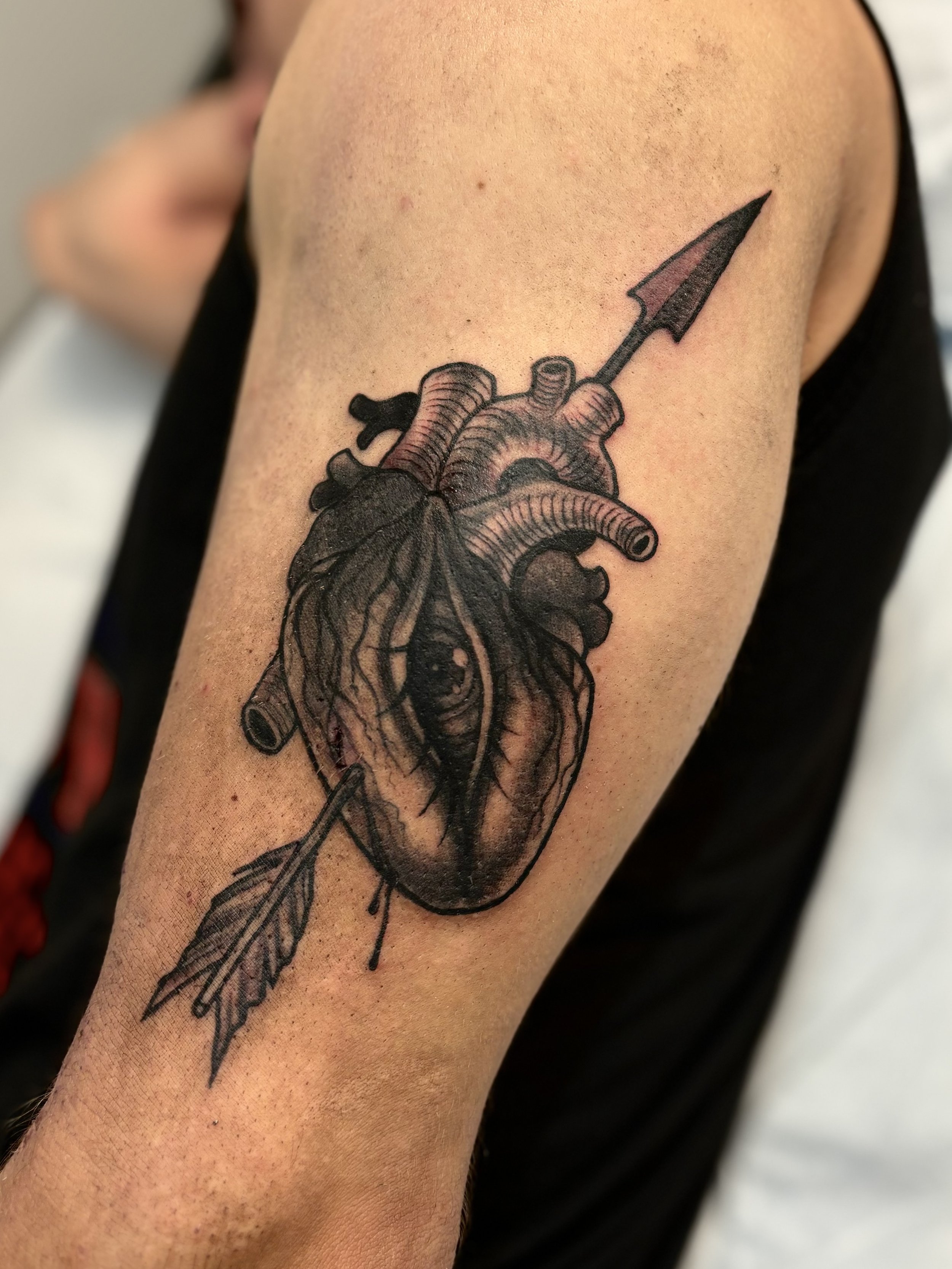 Tattoo of a human heart with an arrow through it, and an eye inside the heart, with a feather at the bottom.