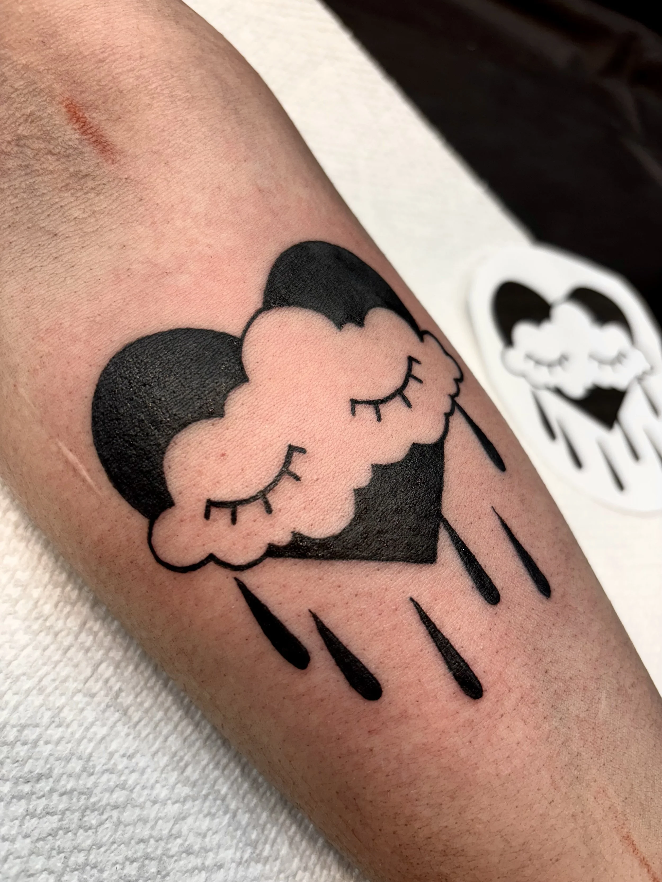 Tattoo of a black heart with a raincloud that has closed eyes.