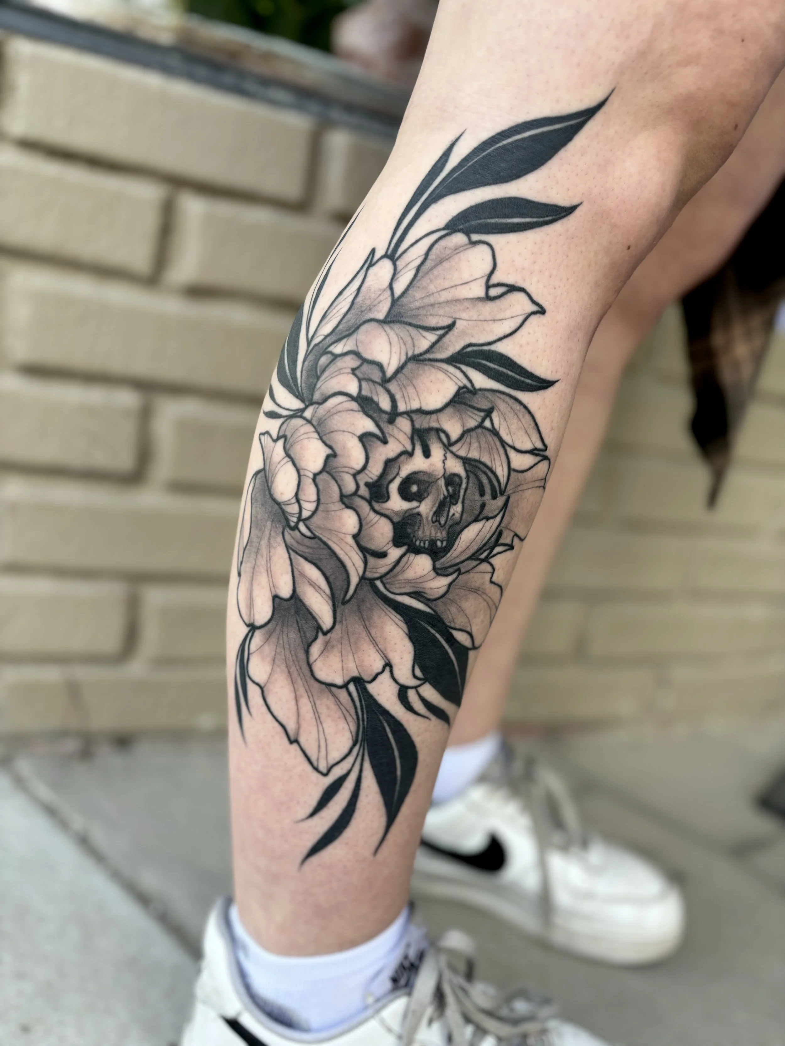 Tattoo of a skull within a large flower and leaves on a person's leg.