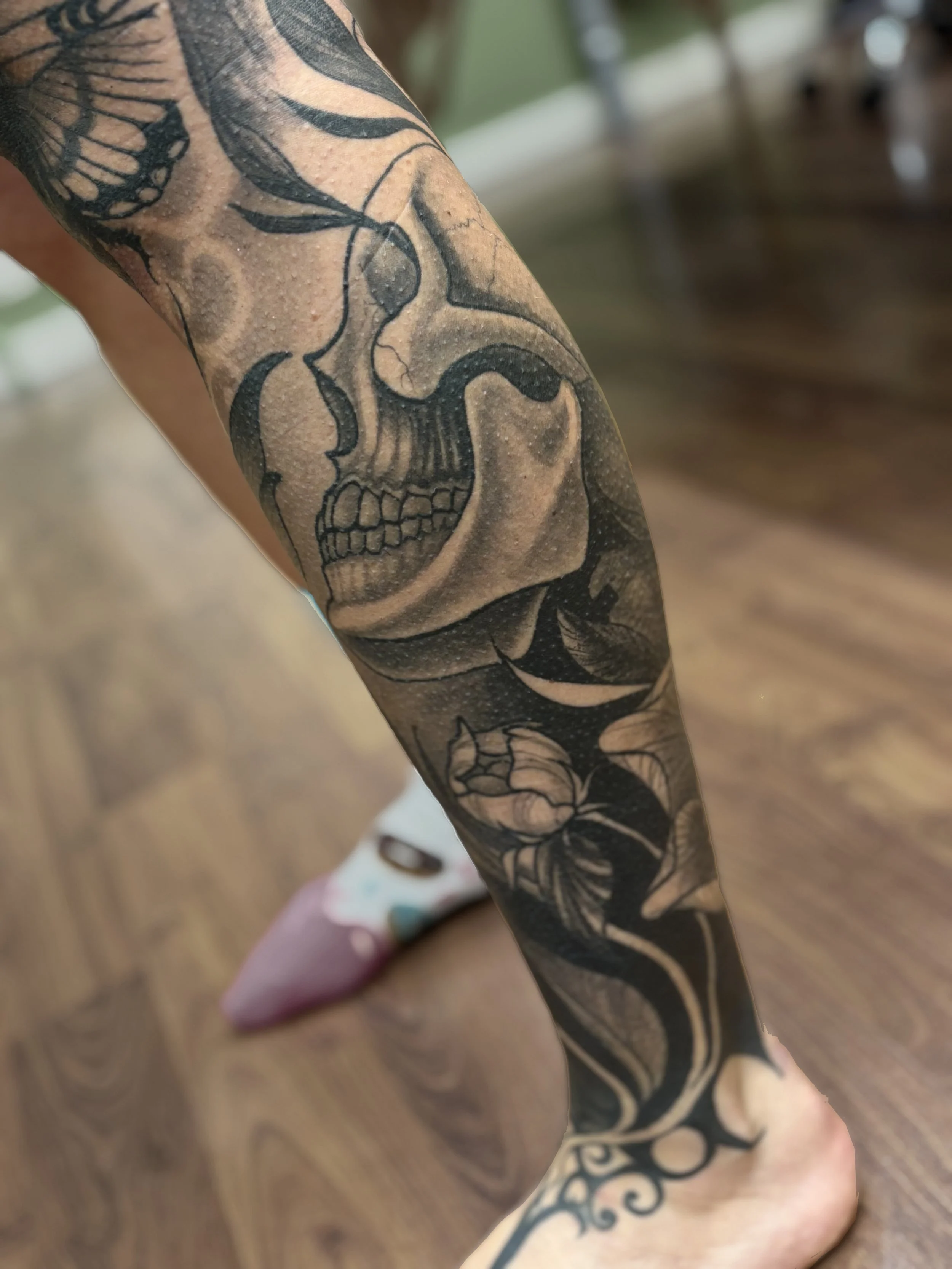 Tattoo of a skull and floral design on a person's arm and leg.