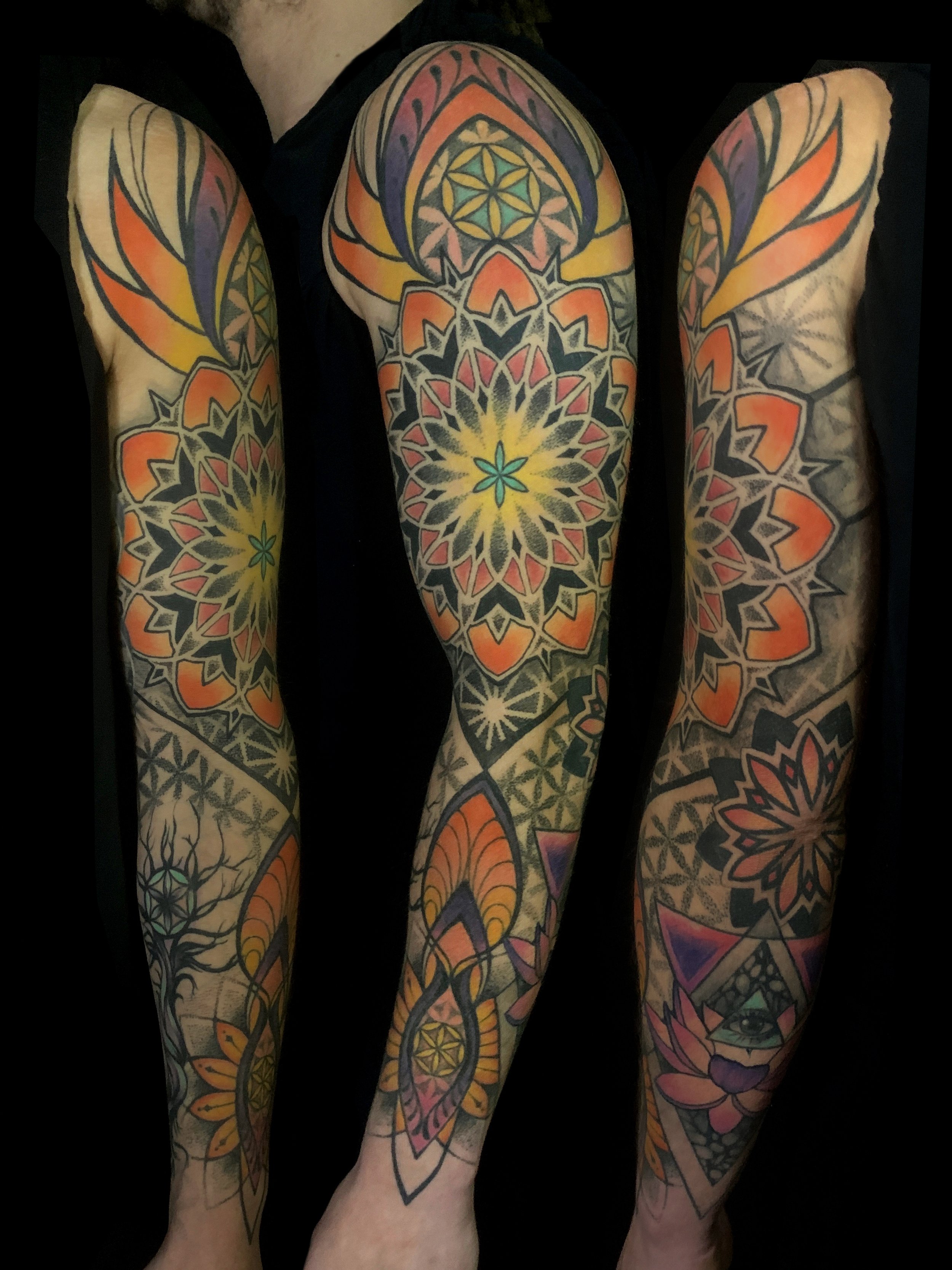Colorful full-sleeve tattoos on a person's arms, featuring geometric patterns, floral motifs, and an eye design, with vibrant orange, yellow, purple, and green hues.
