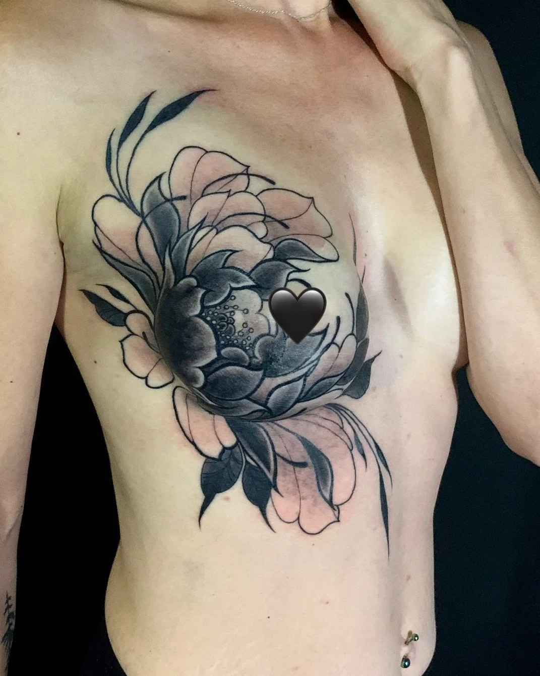 Tattoo of a large peony flower on a person's chest with a black heart shape at the center.