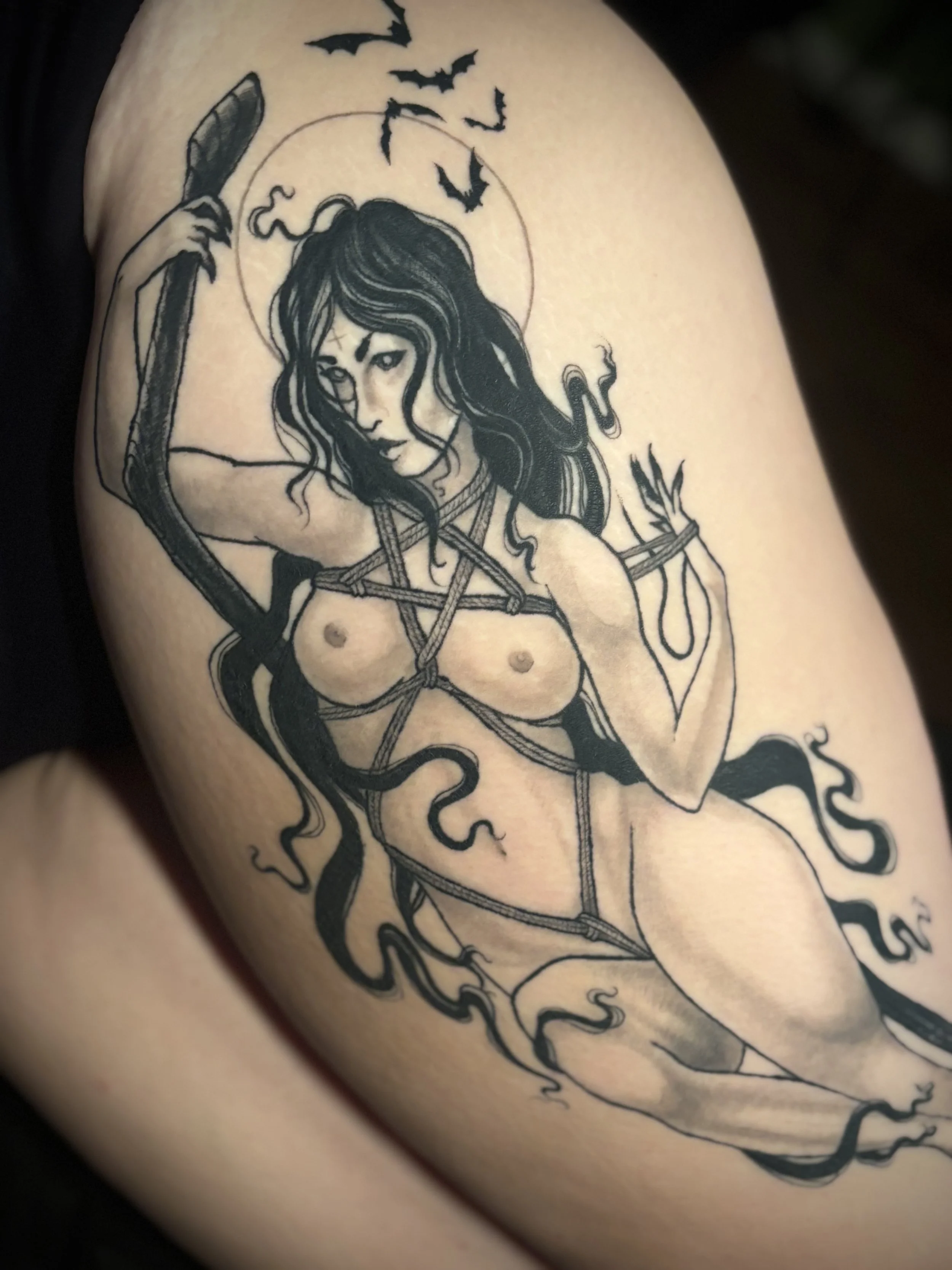Tattoo of a witch tied in shibari knots with long hair and bats flying in the background.
