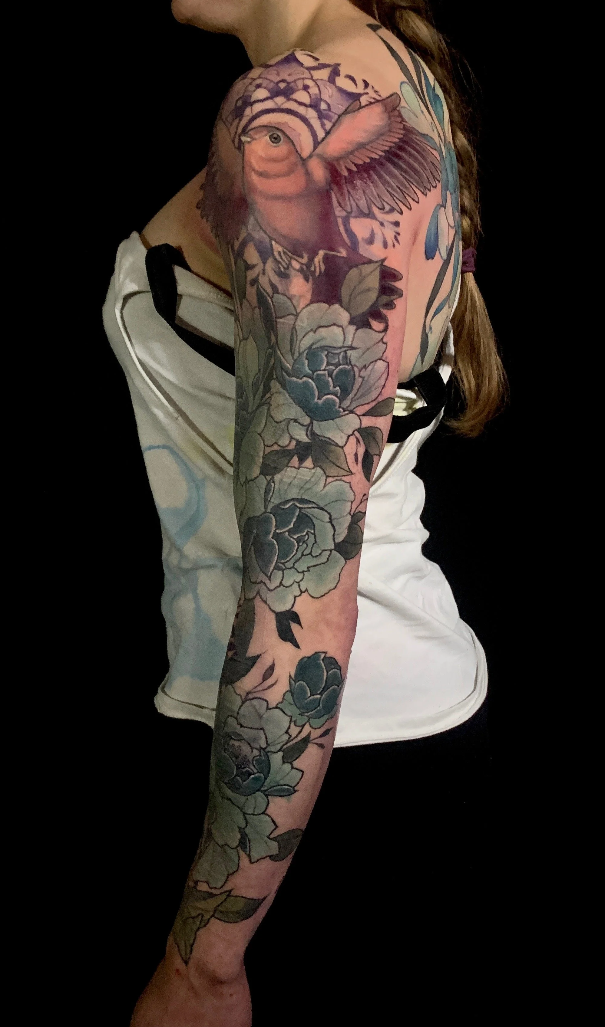 A detailed colourful floral tattoo sleeve, featuring peonies, and a bird with outstretched wings on the upper arm.