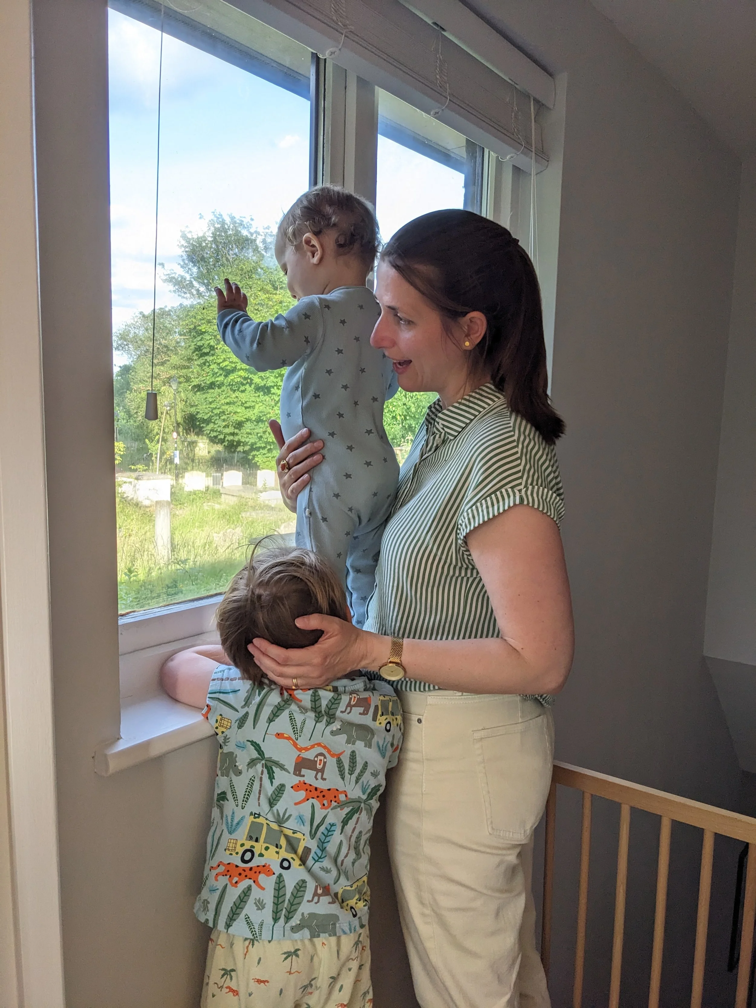 A mum with her baby and toddler by the window, engaging playfully, showcasing family bonding and the support offered to parents preparing for baby number two after Antenatal Courses E17.