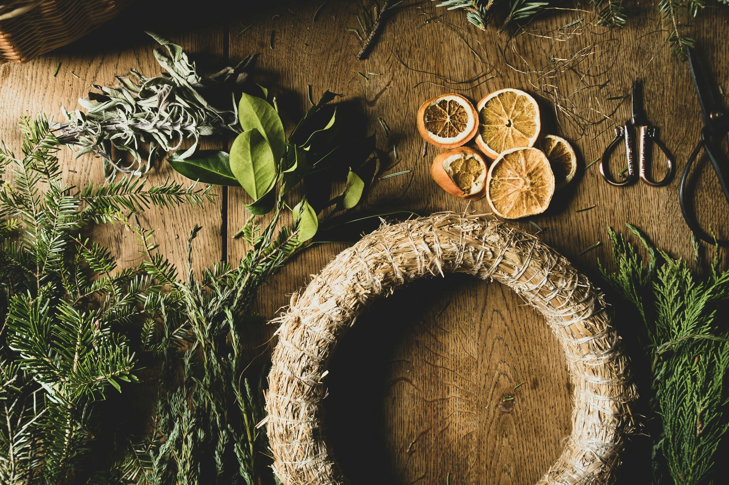 Materials for a Christmas wreath-making workshop in Walthamstow, including evergreen branches, oranges, leaves, and string, laid out on a rustic table.