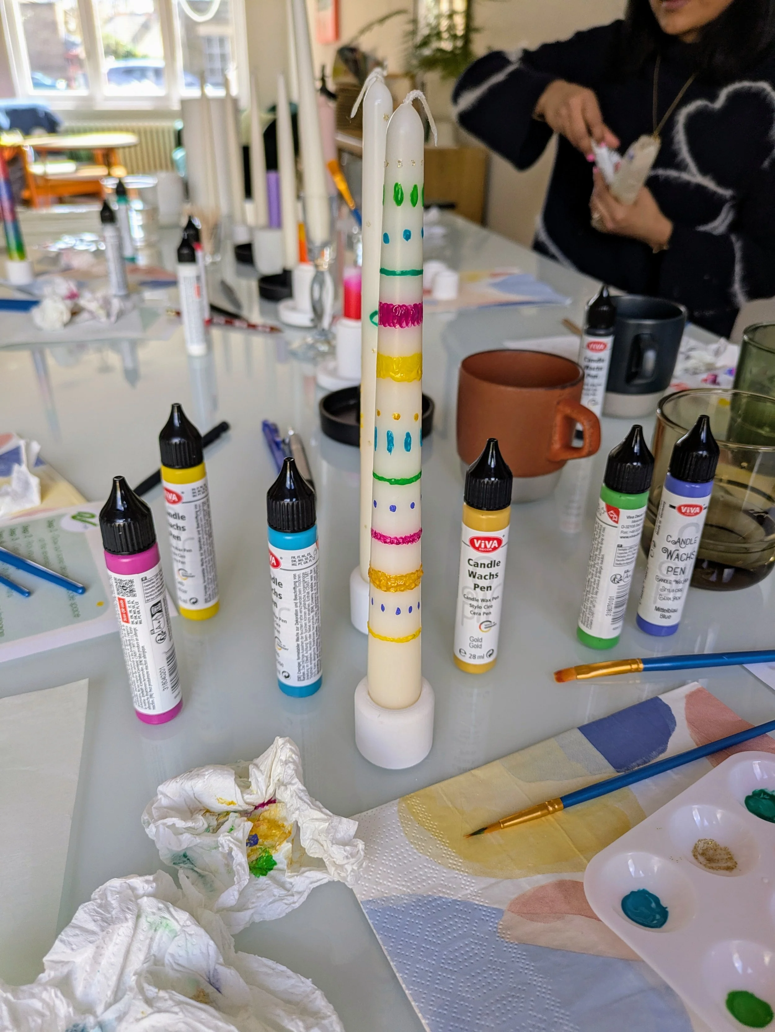 Hand-painted white candle with colourful design on a table, from a candle painting class E17 for parents.