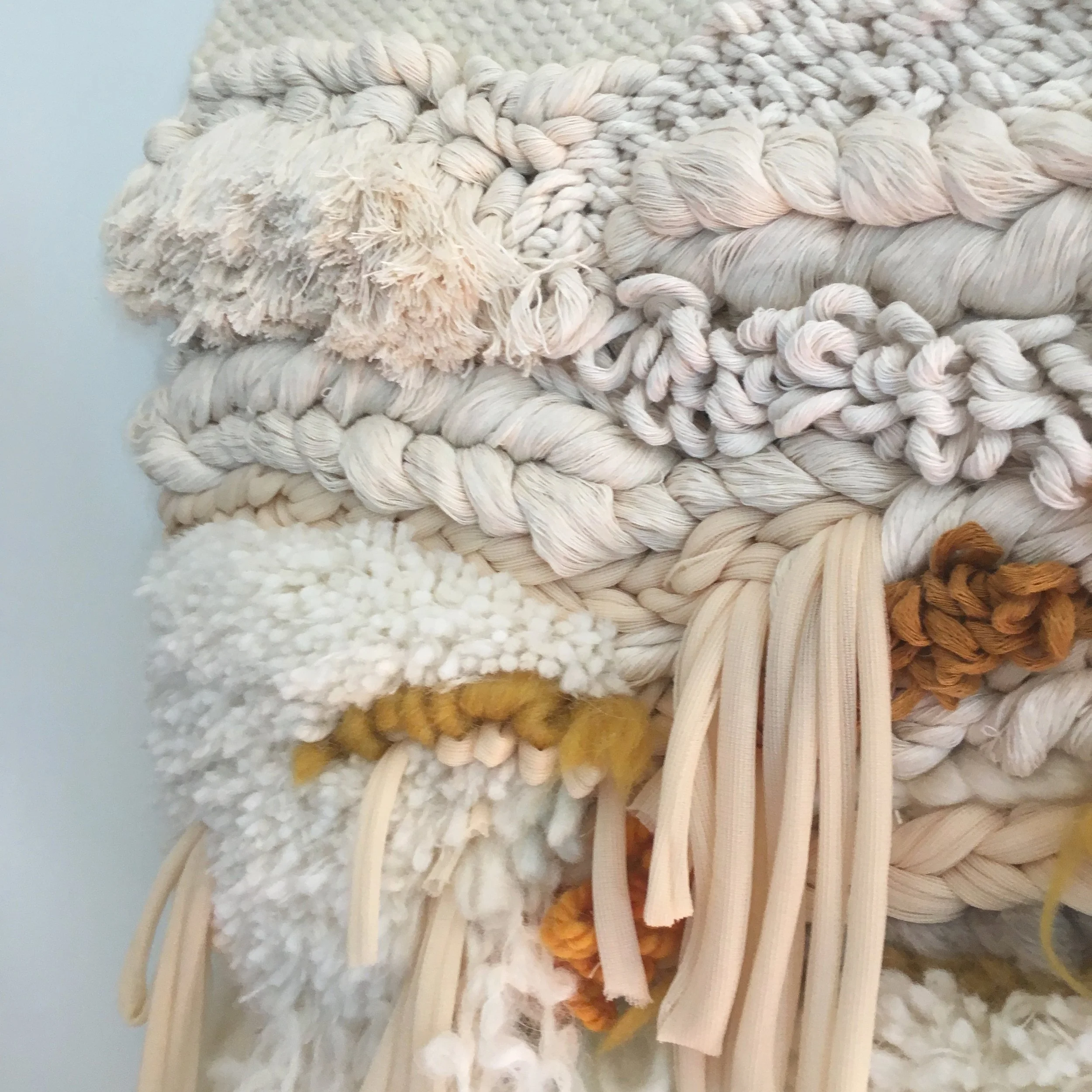 Close-up of textured handmade fiber art using various yarns in neutral tones with mustard accents.