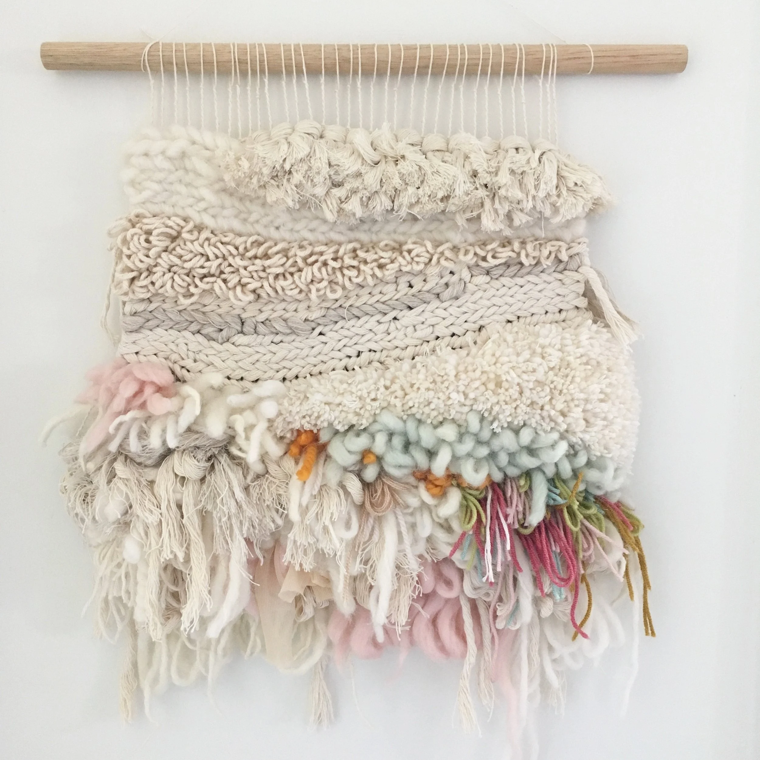Handmade textile wall hanging with various yarn textures and colors on a wooden rod.