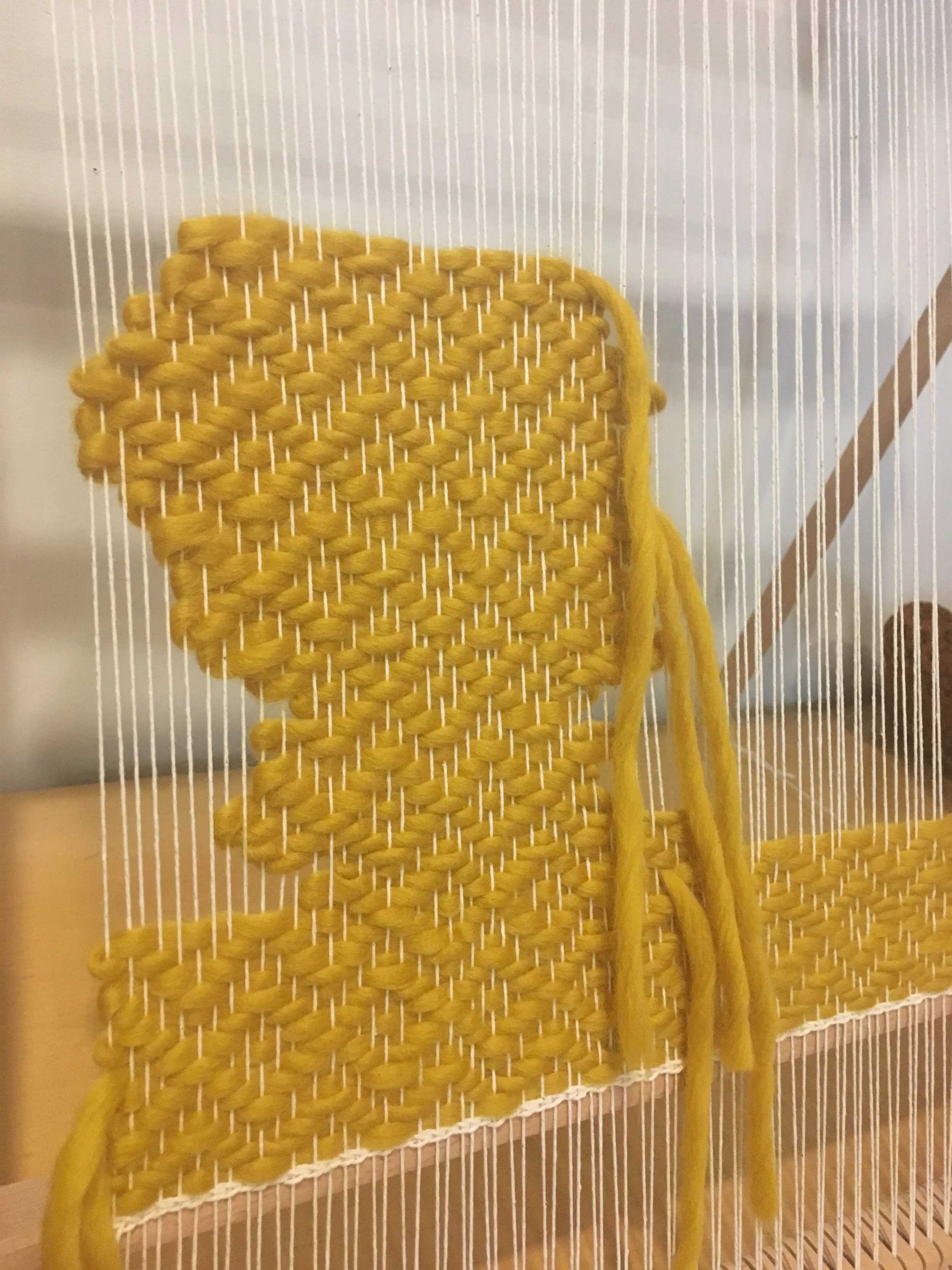 Close-up of a weaving loom with yellow yarn creating a textured pattern on white warp threads.