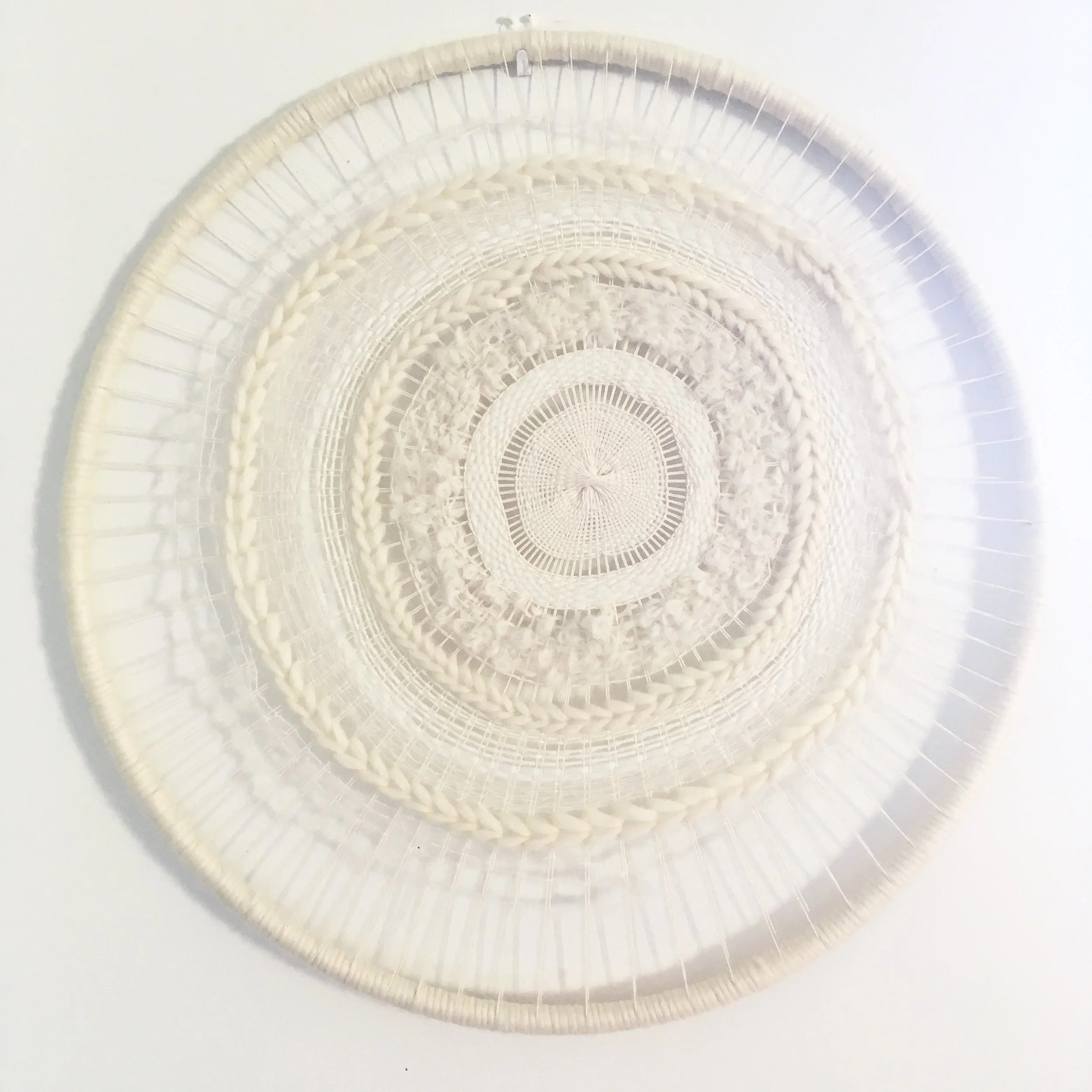 Large white woven circular wall hanging with intricate patterns.