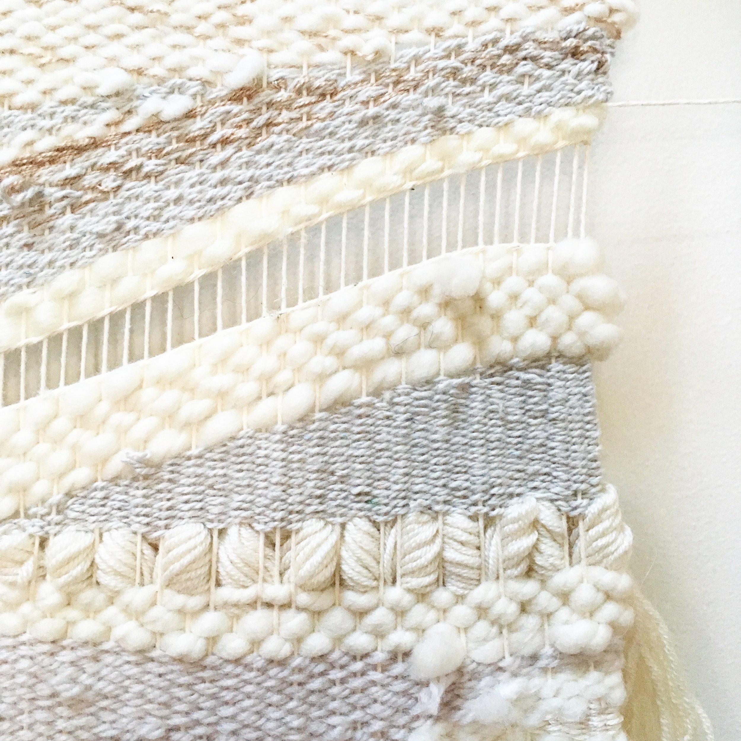 Close-up of a textured woven fabric with various weaving patterns in white and beige hues.