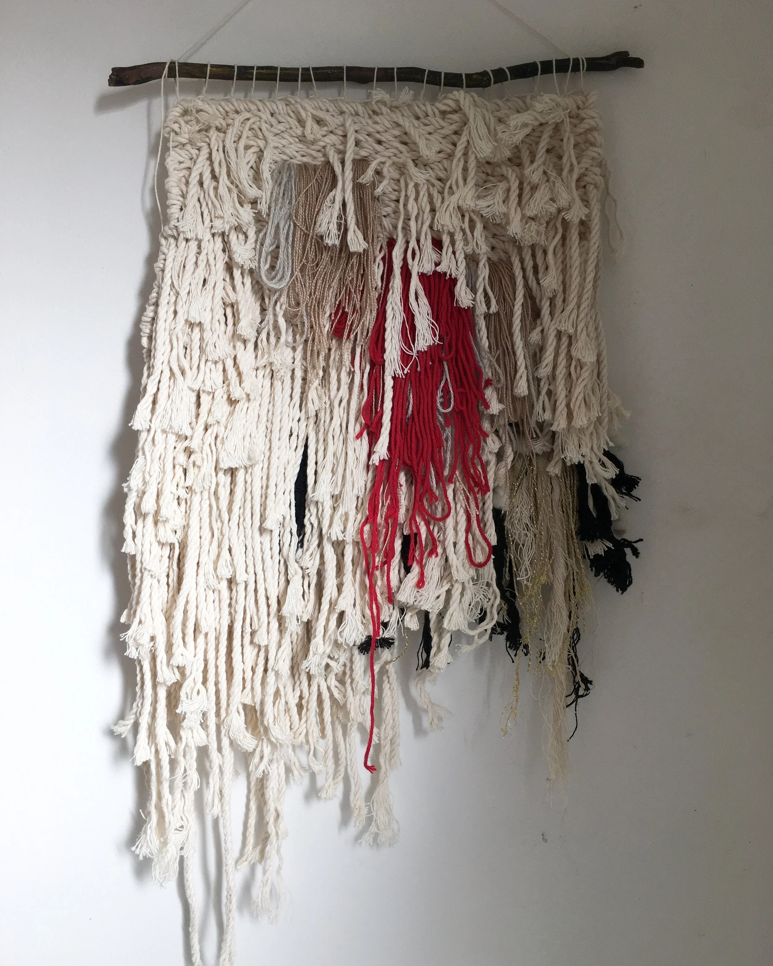 Handmade macramé wall hanging with natural fibers and red accents.