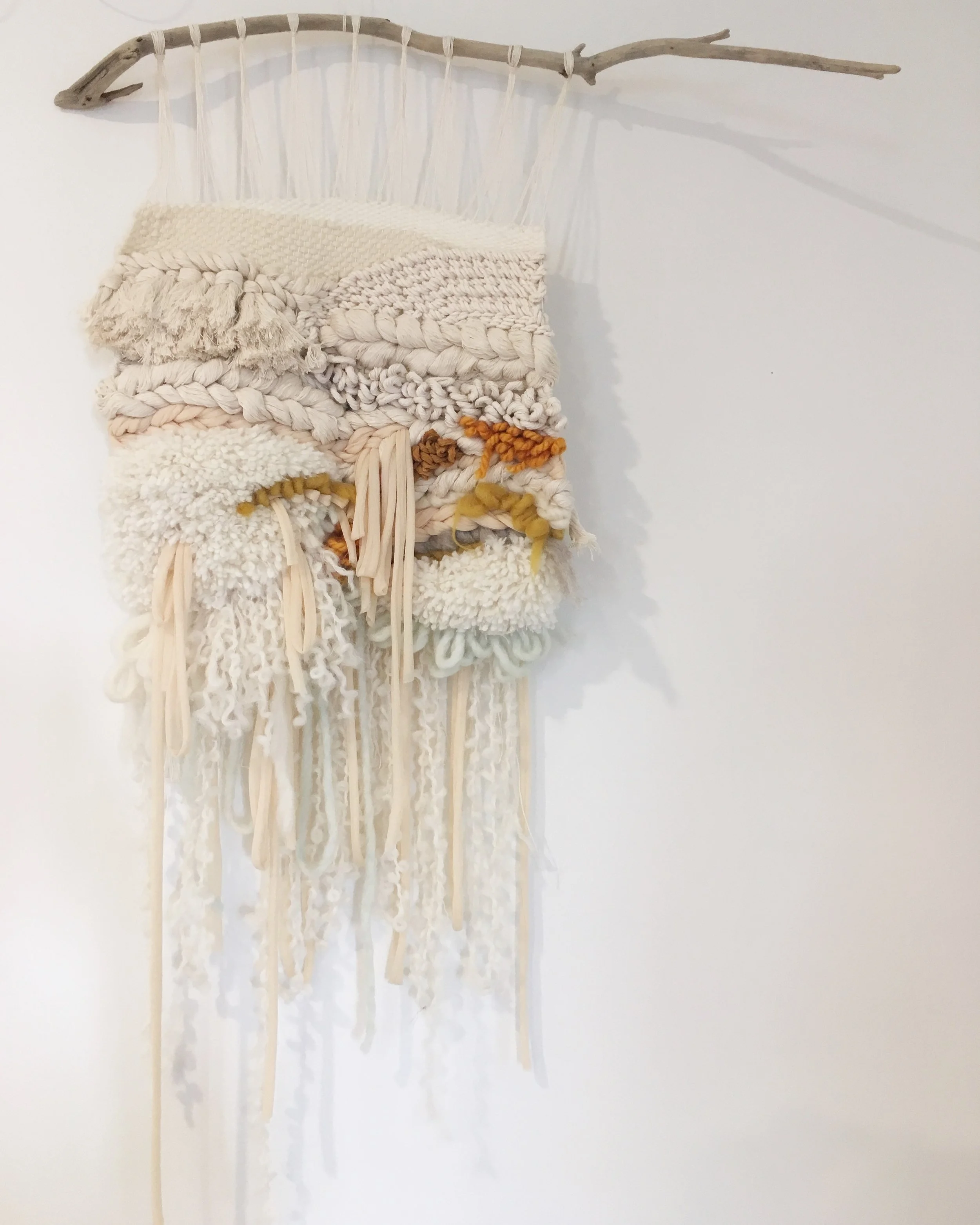 Textured wall hanging with mixed fibers on a branch