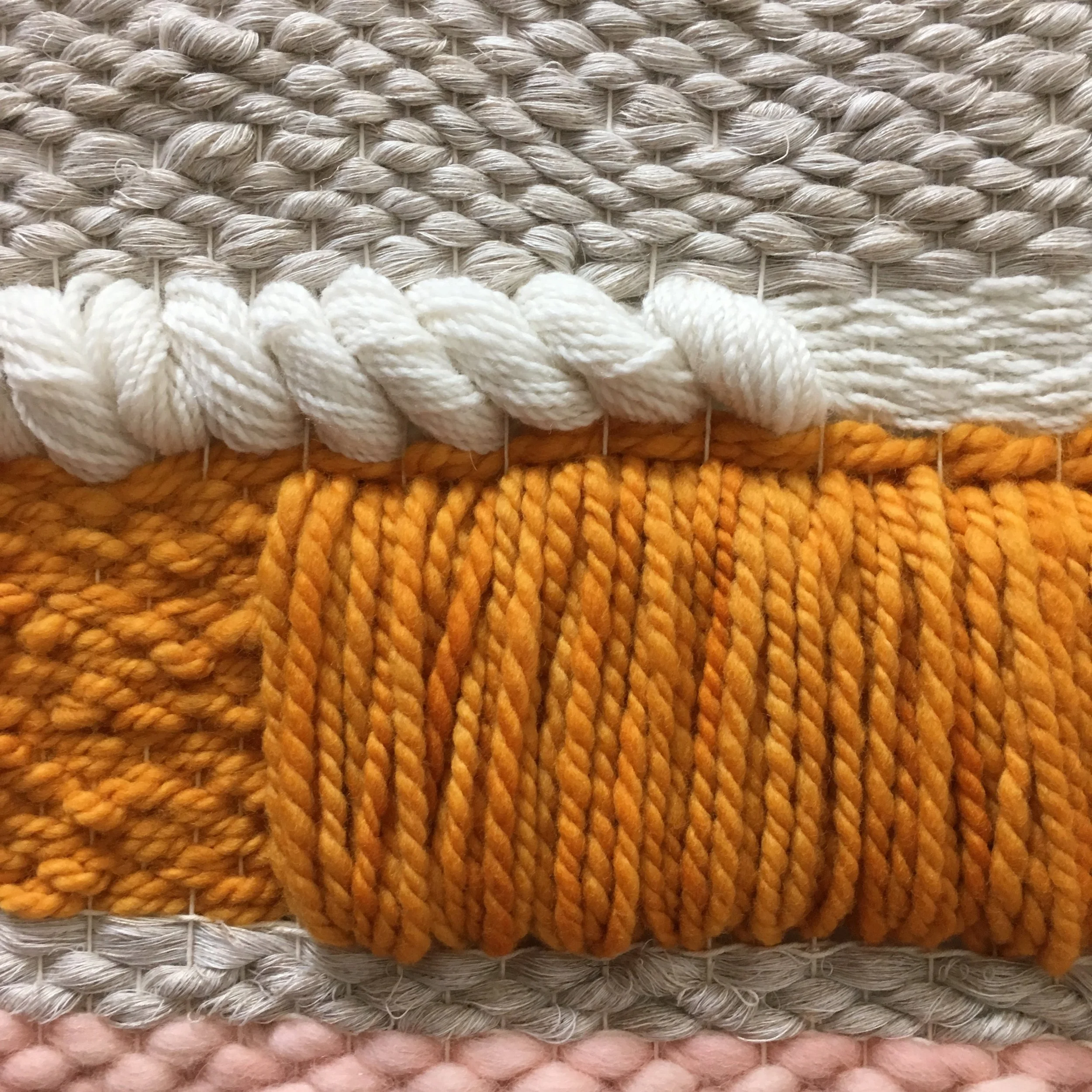 Close-up of woven textile with orange, white, gray, and pink threads in various textures and patterns.
