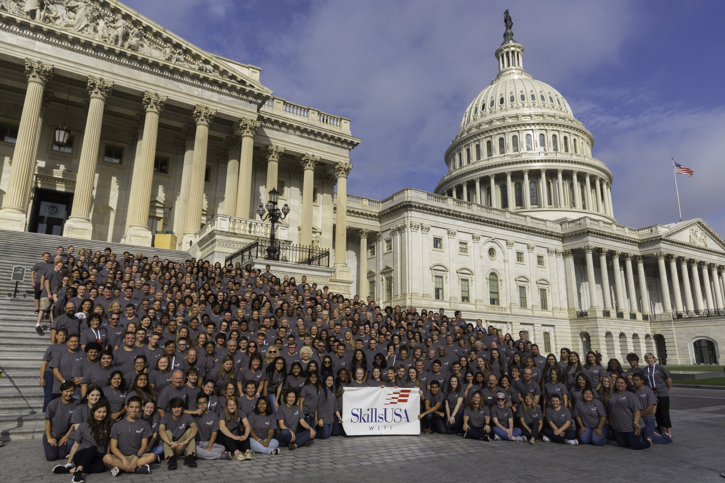 A group in dark grey shirts poses with a SkillsUSA banner on the Capitol steps.