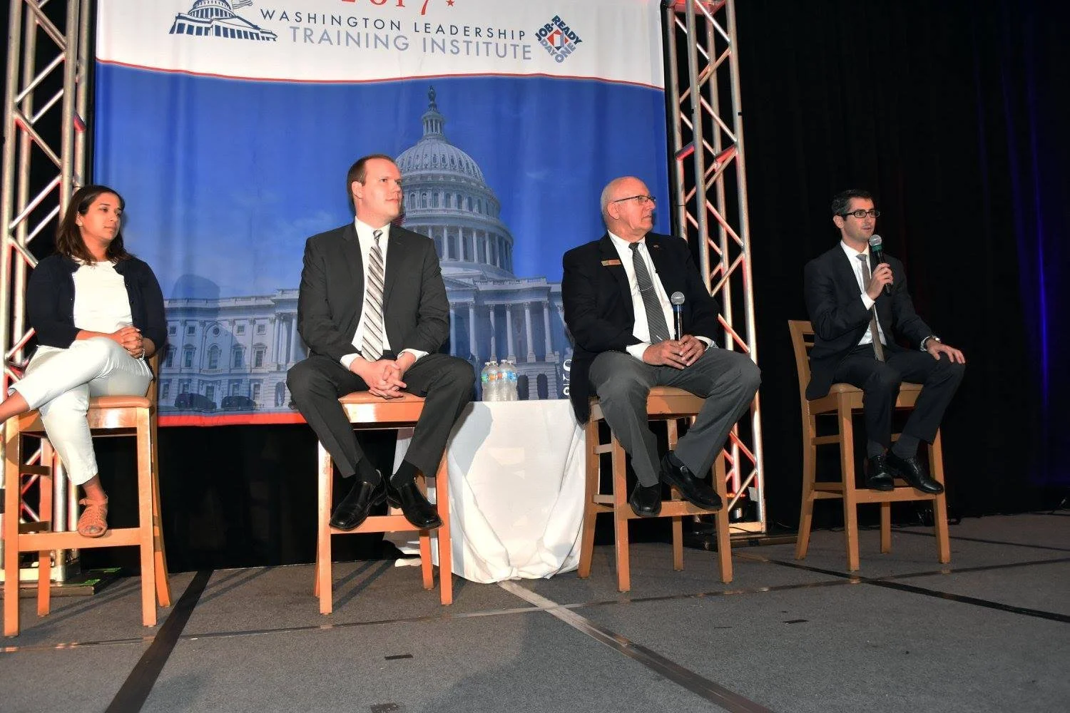 Panelists speak on stage at a leadership conference with a Capitol-themed backdrop.