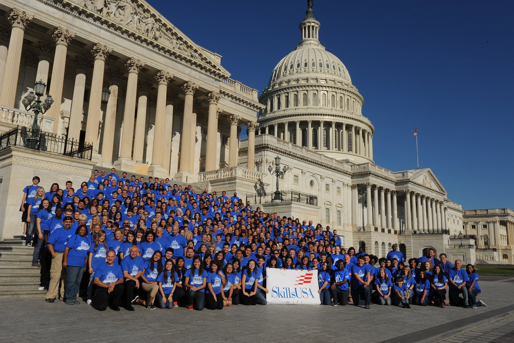 A group of blue-shirted SkillsUSA participants poses with a banner in front of the Capitol.
