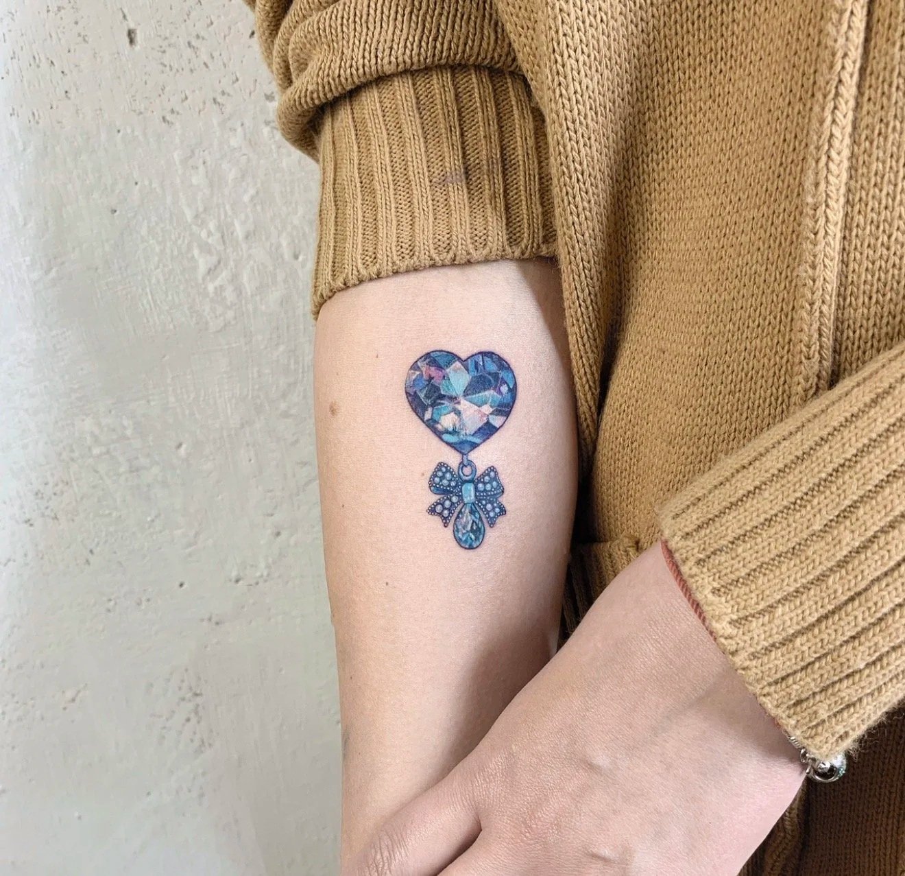 Blue heart gemstone tattoo with bow on inner arm