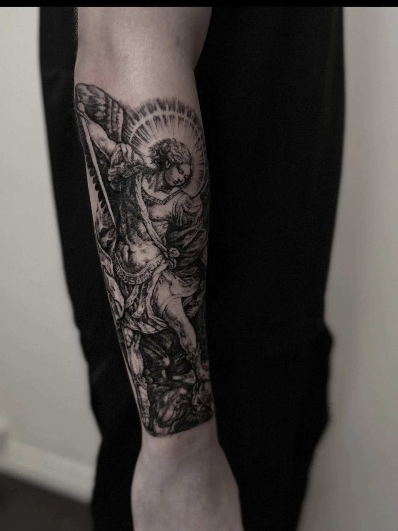 Black and gray tattoo of a warrior with a shield and sword on a person's arm.