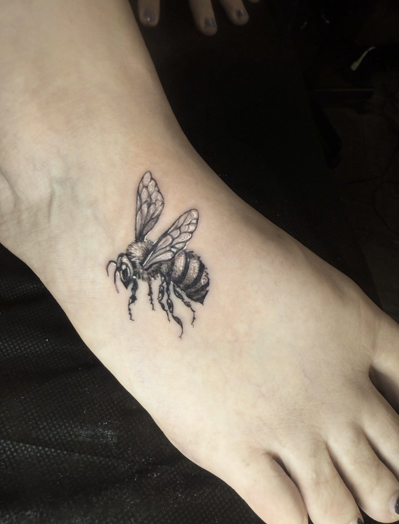 Black and gray tattoo of a bee on a person's skin.
