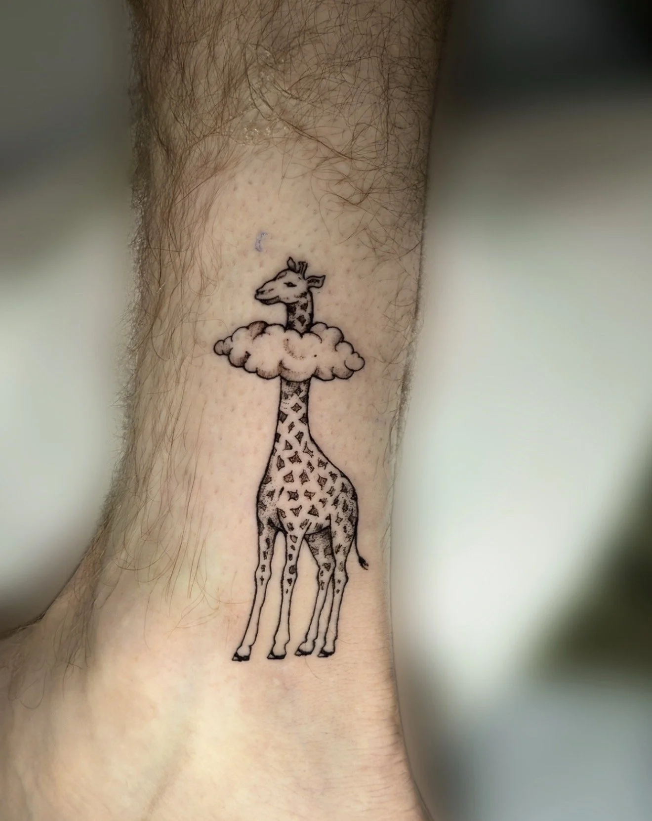 Tattoo of a cartoon giraffe with a long neck standing next to a cloud, on a person's leg.