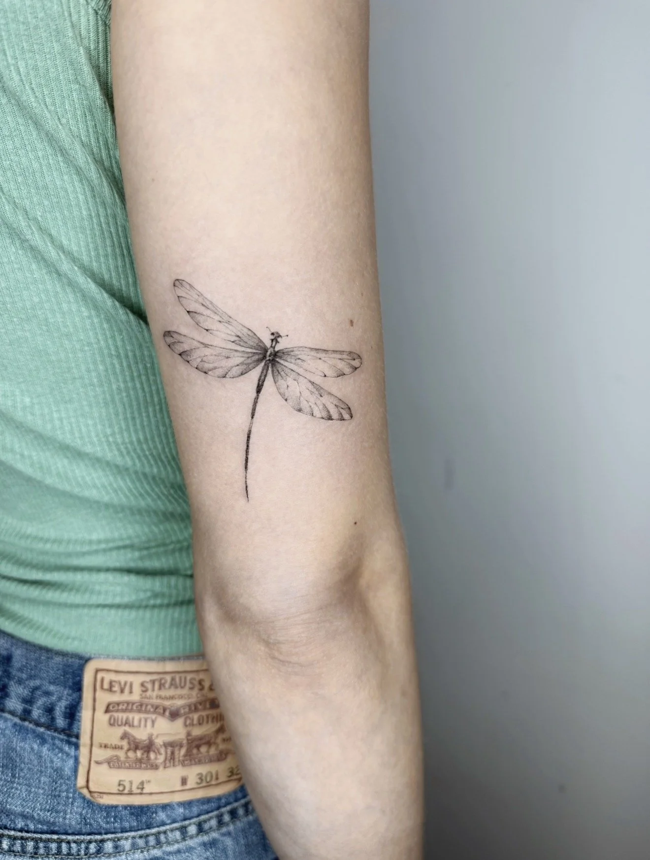 A person's forearm with a detailed black and gray line-drawn tattoo of a dragonfly.