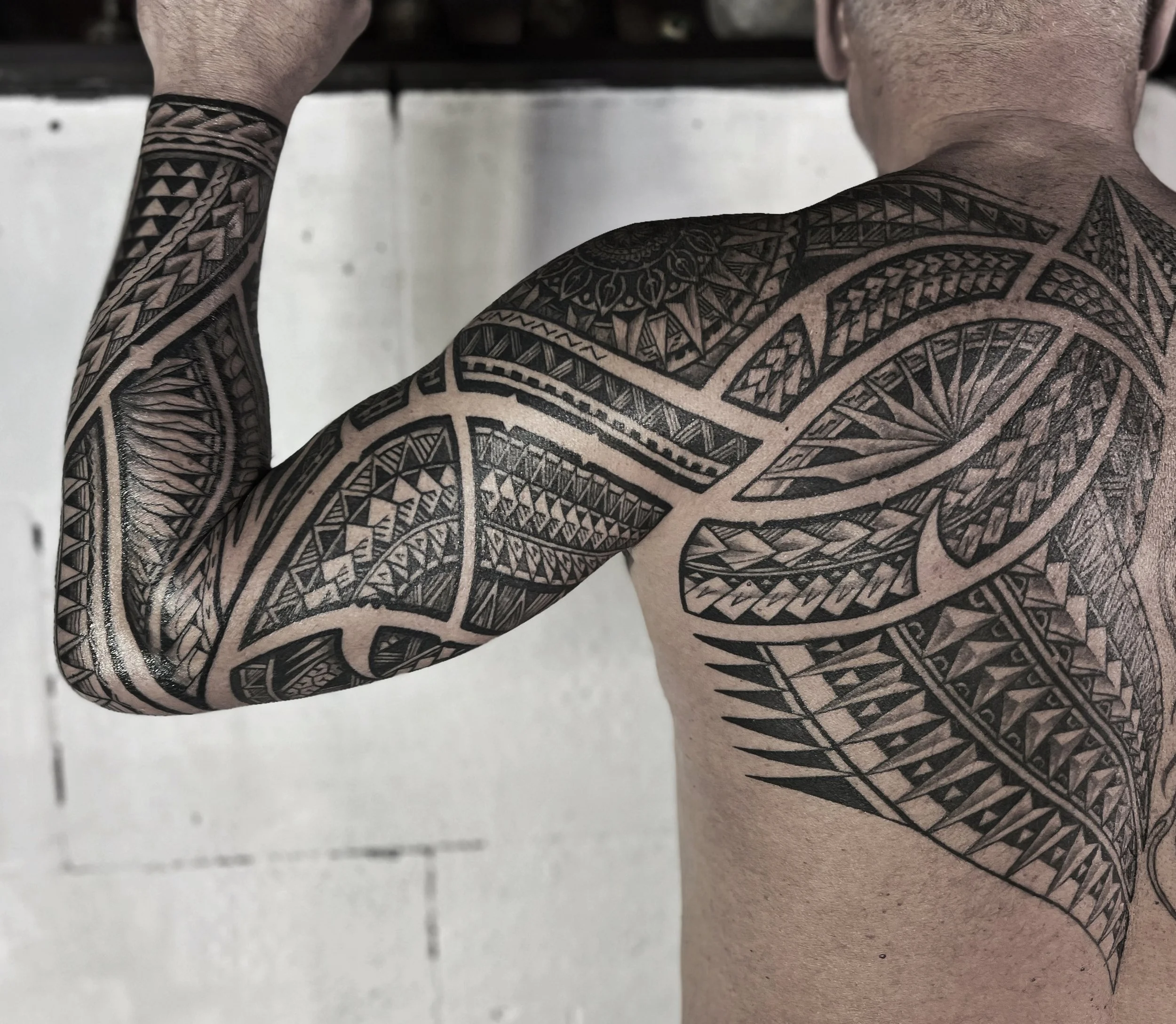 A person with extensive traditional tribal tattoos covering their arm, shoulder, and upper back, with detailed black geometric and patterned designs.
