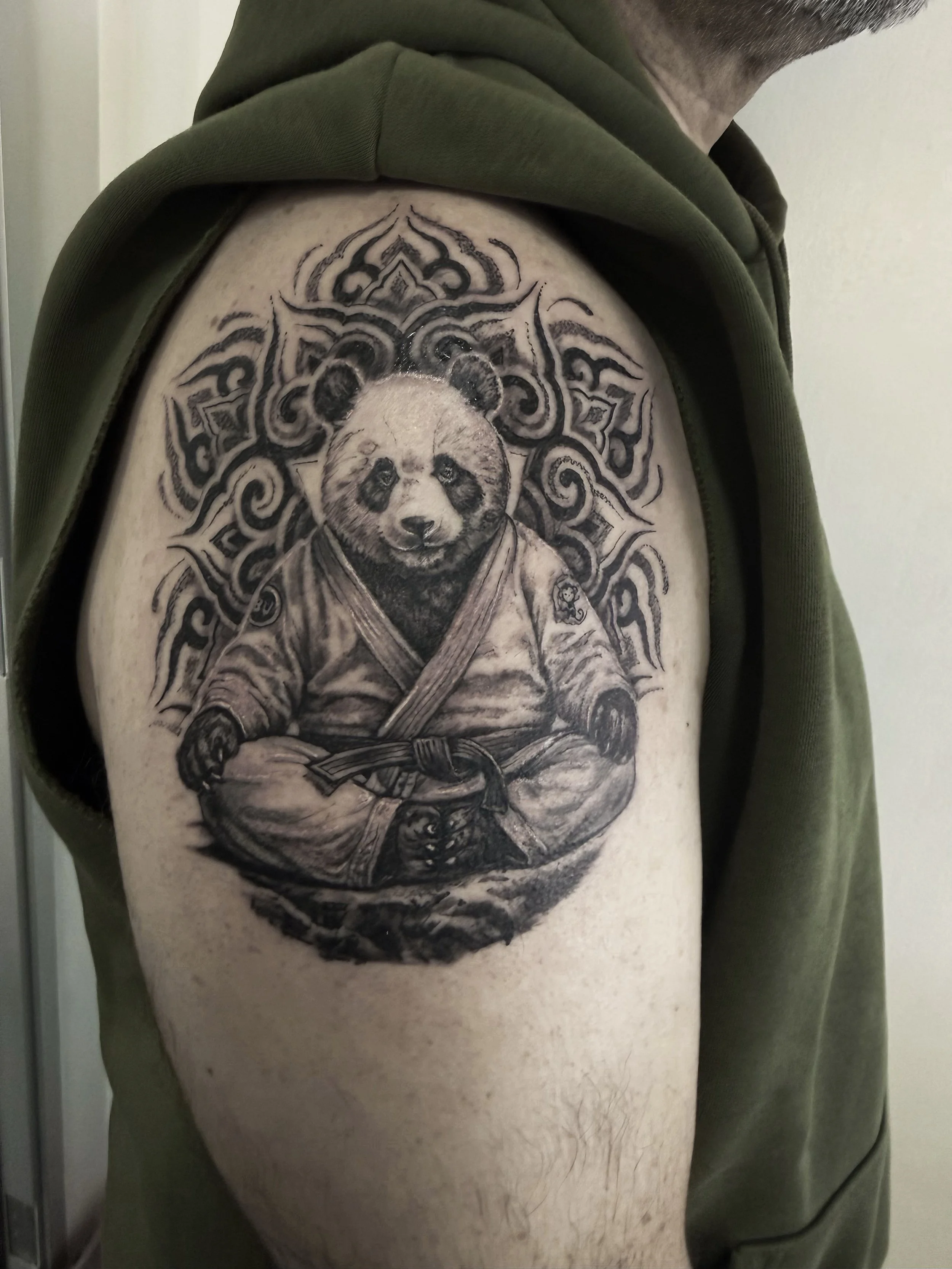A black and grey tattoo of a panda bear in traditional Japanese clothing on a person's upper arm, with ornate decorative elements surrounding it.
