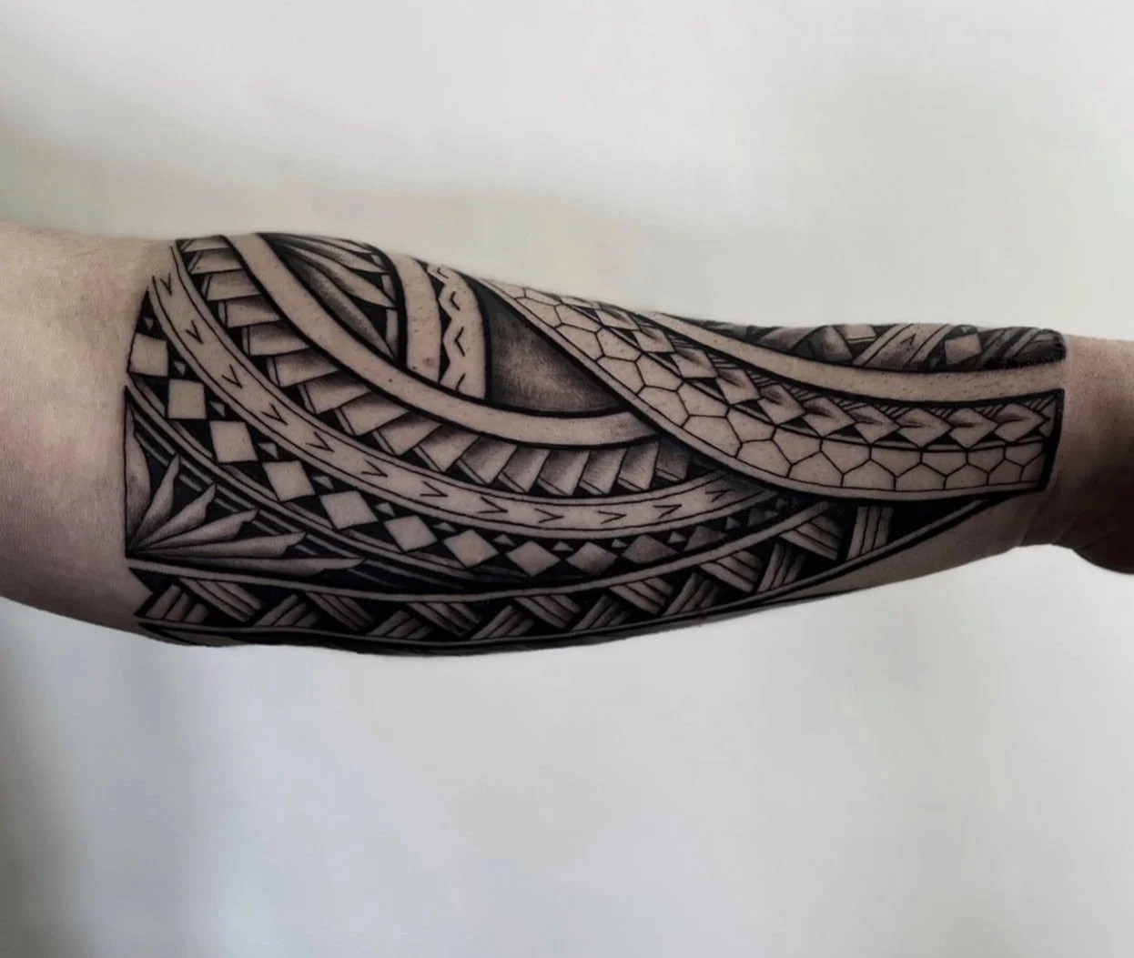 Black and gray Polynesian tribal tattoo on a person's arm with geometric patterns and intricate linework.