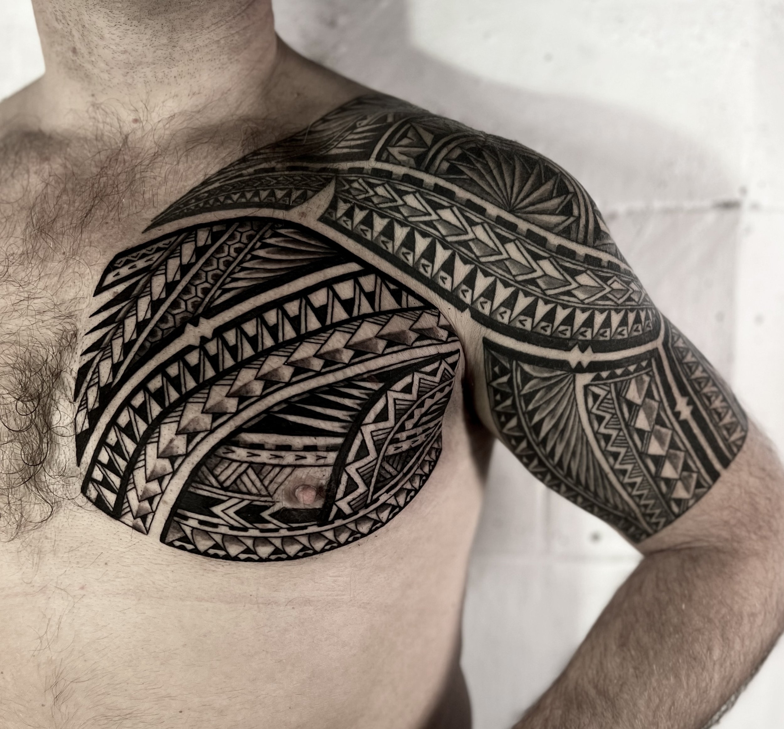 Close-up of a person's shoulder displaying intricate black tribal-style tattoo art covering the upper arm and shoulder area.