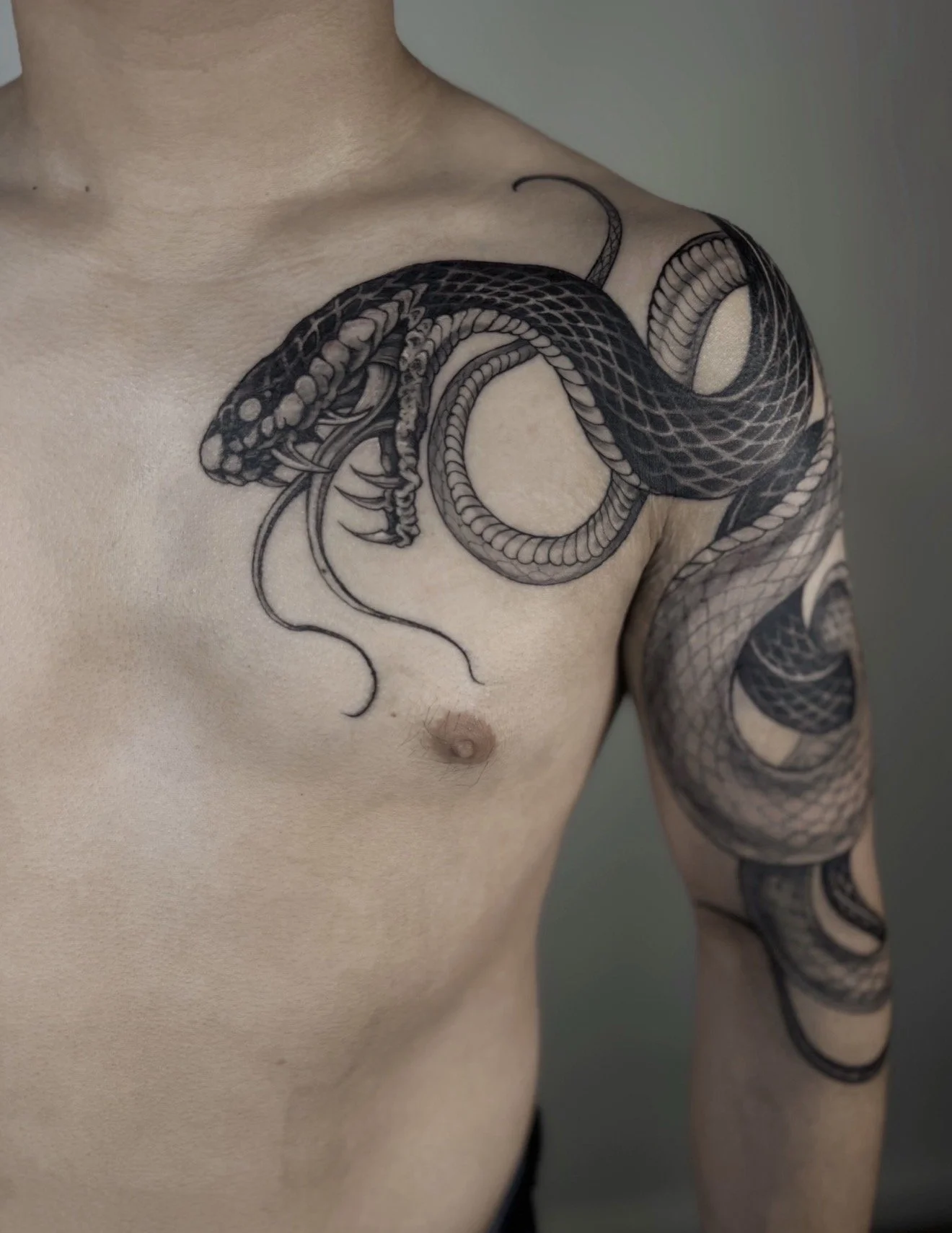 Close-up of a man's upper torso featuring a detailed black and gray snake tattoo that wraps around his shoulder and arm.