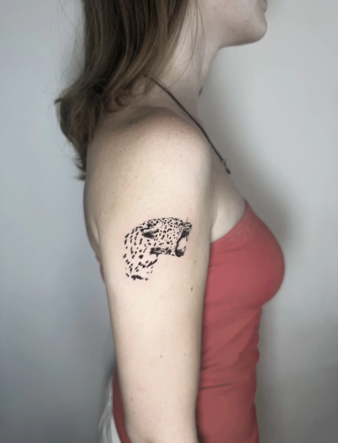 A woman with shoulder-length brown hair wearing a red tank top, showing a black leopard head tattoo on her upper arm.