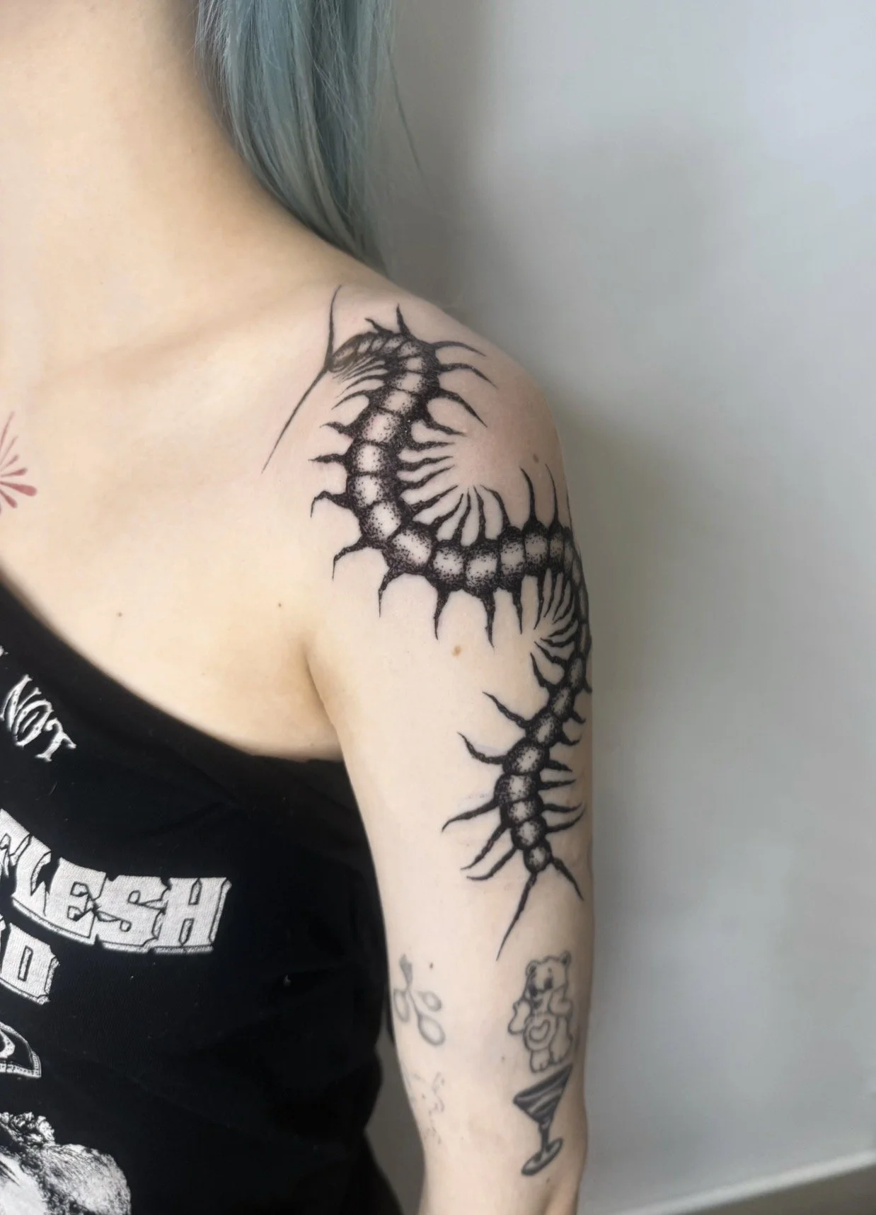 Tattoo of a curled centipede on person's shoulder and upper arm.
