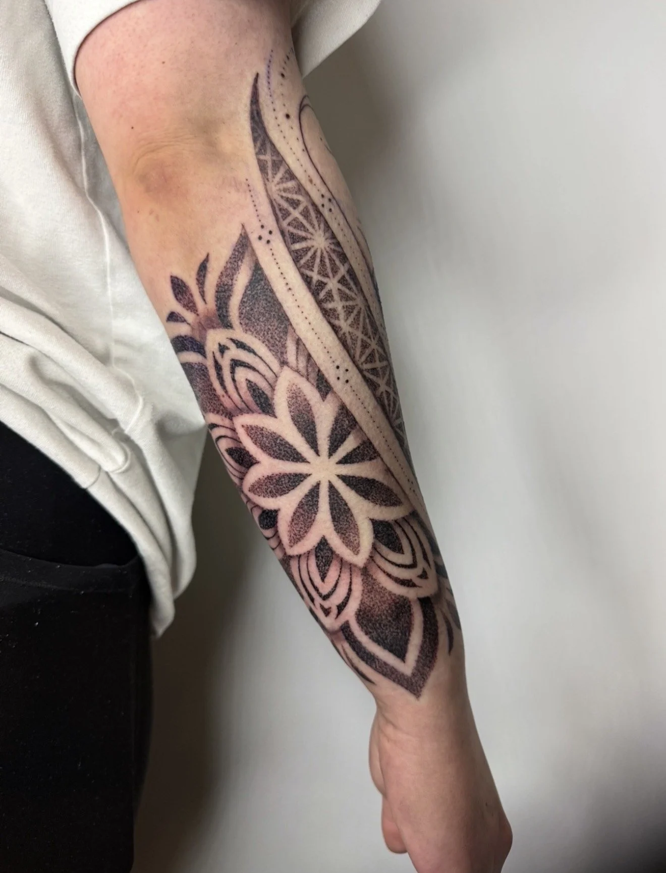 Tattooed arm with geometric and floral designs holding a person's hand.