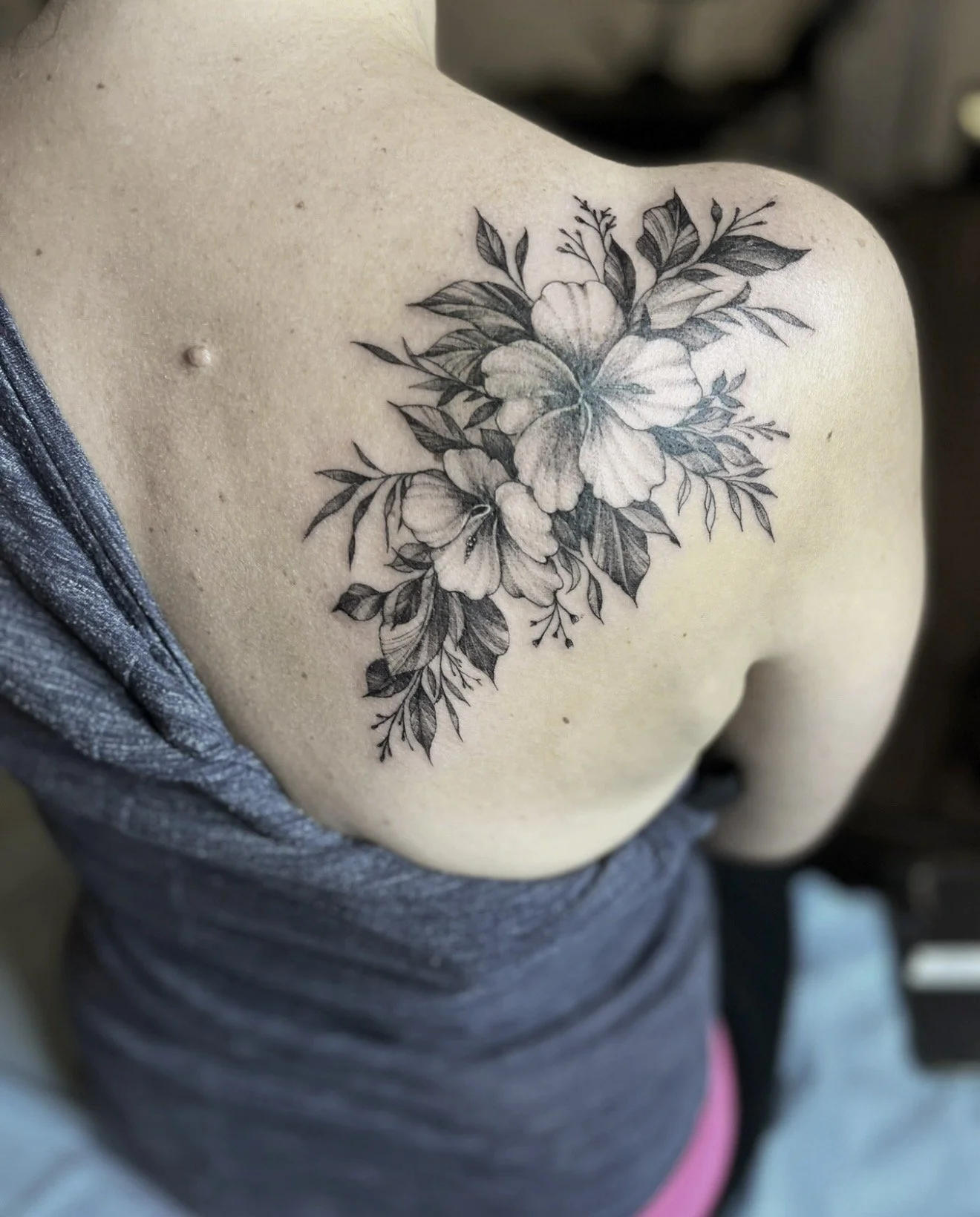 Black and gray floral tattoo on a person's shoulder, featuring large flowers and leaves.
