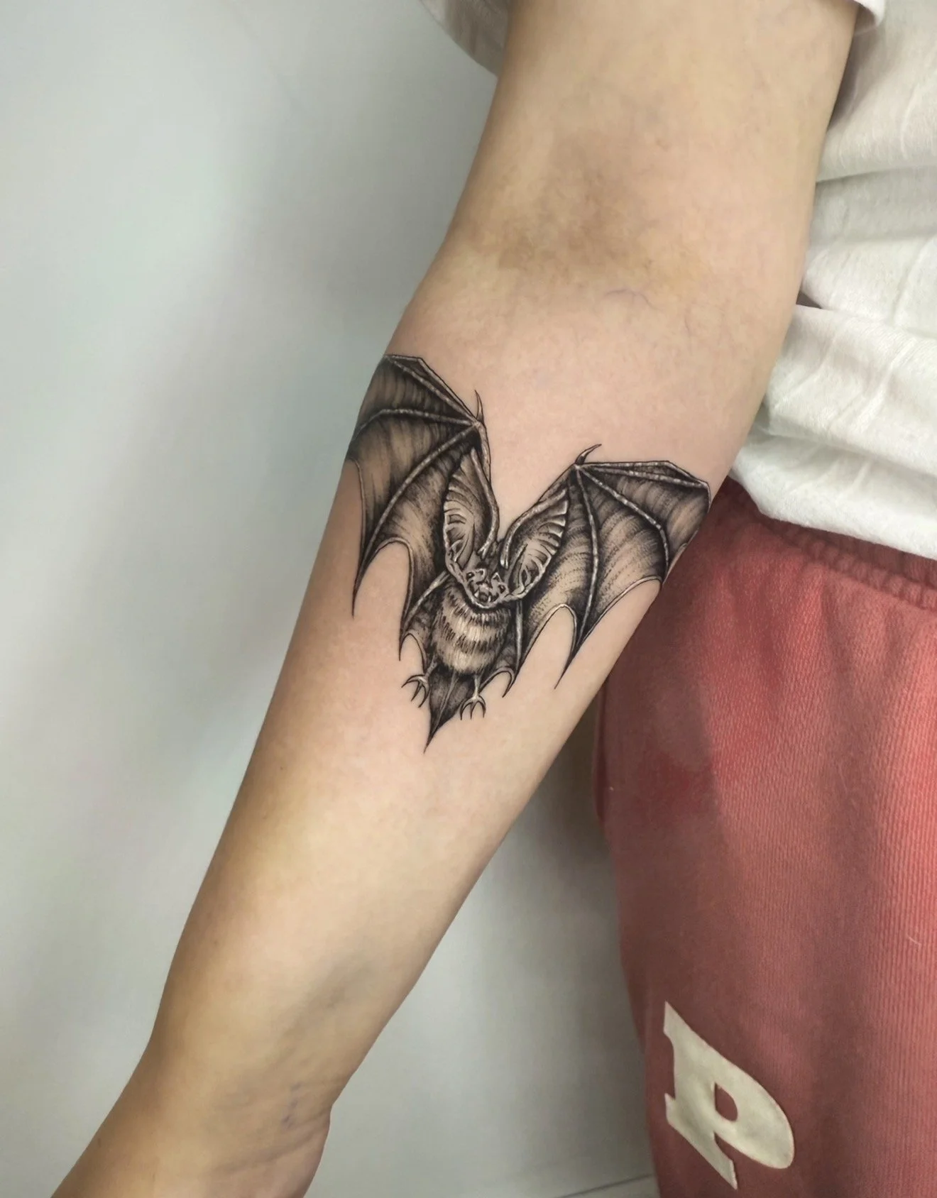 Black and gray tattoo of a flying bat on a person's forearm.