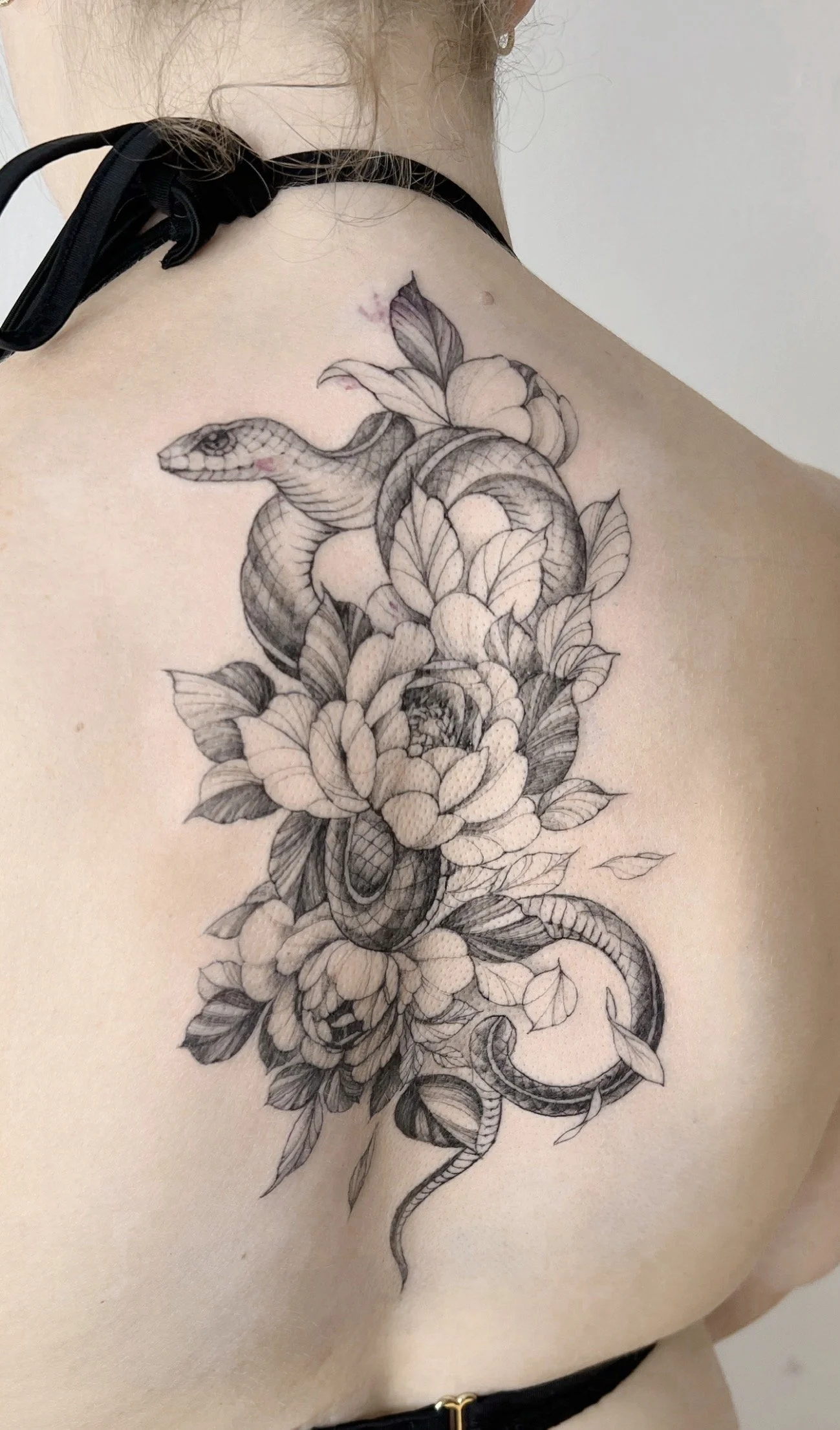 Black and gray tattoo of a snake intertwined with flowers on a person's upper chest and shoulder.
