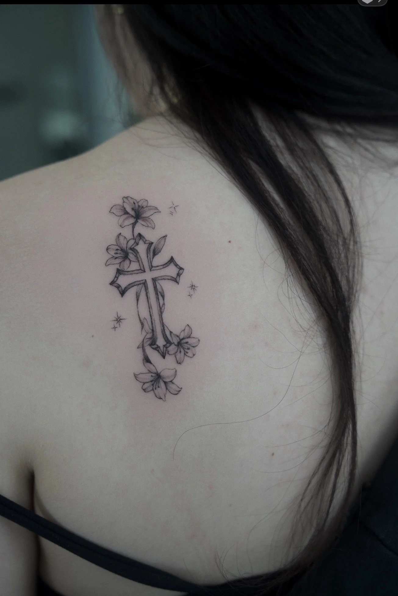 Tattoo of a cross with floral design on someone's shoulder.
