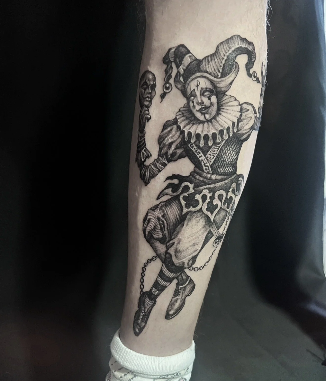Tattoo of a harlequin clown holding a mask on the arm.