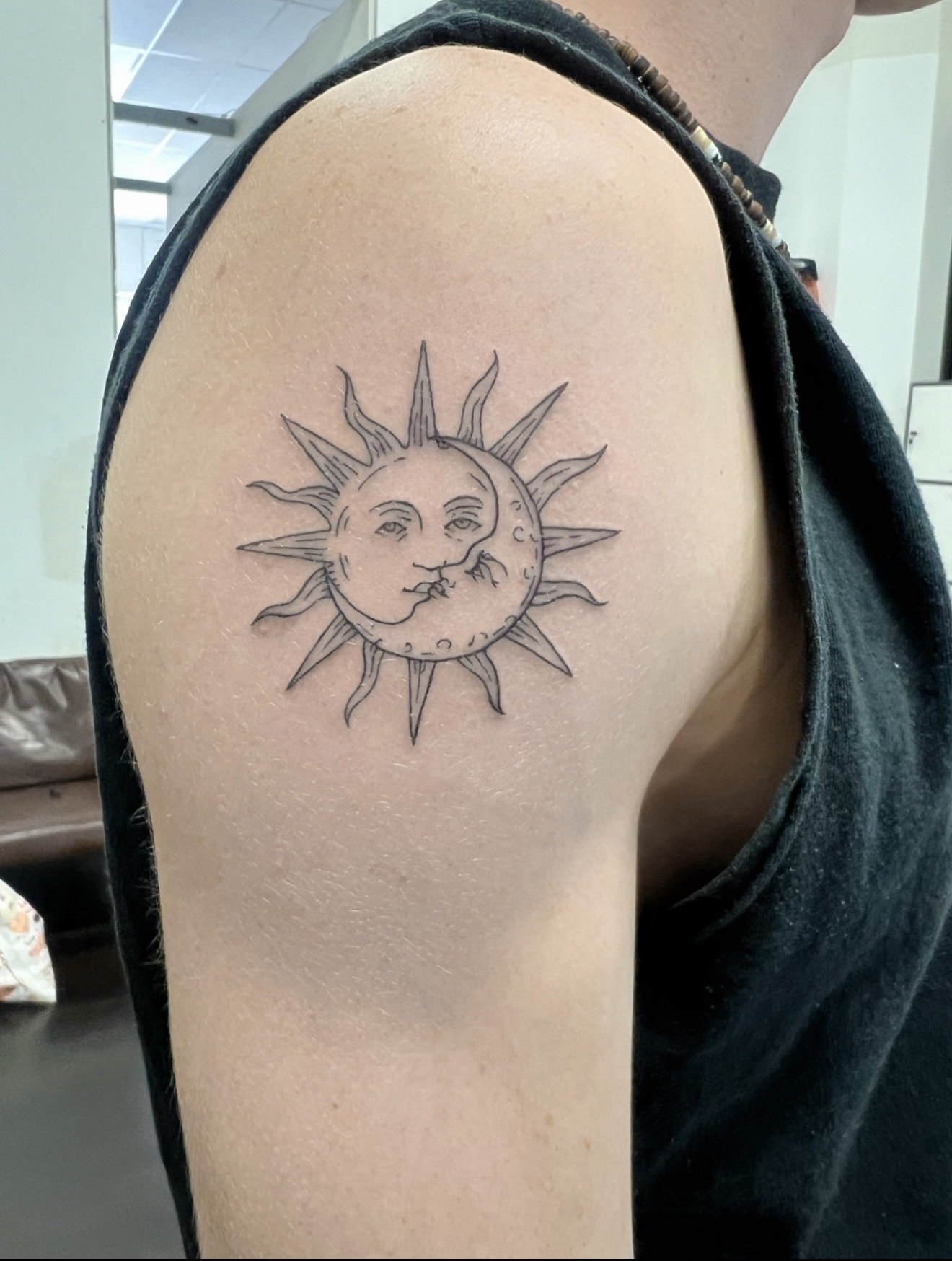 Tattoo of a sun and moon face design on a person's upper arm.