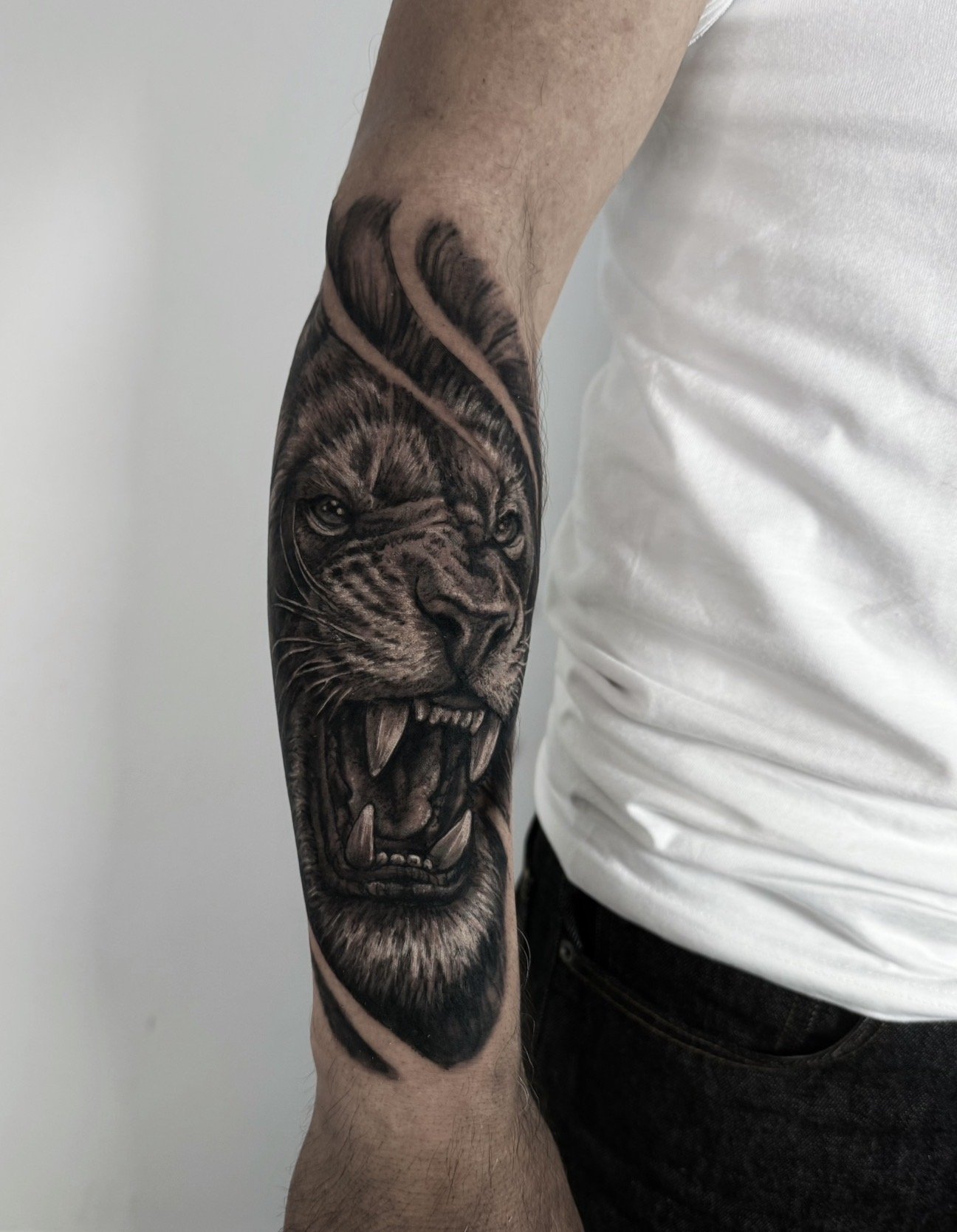 Black and grey tattoo of a roaring lion's face on a person's forearm.