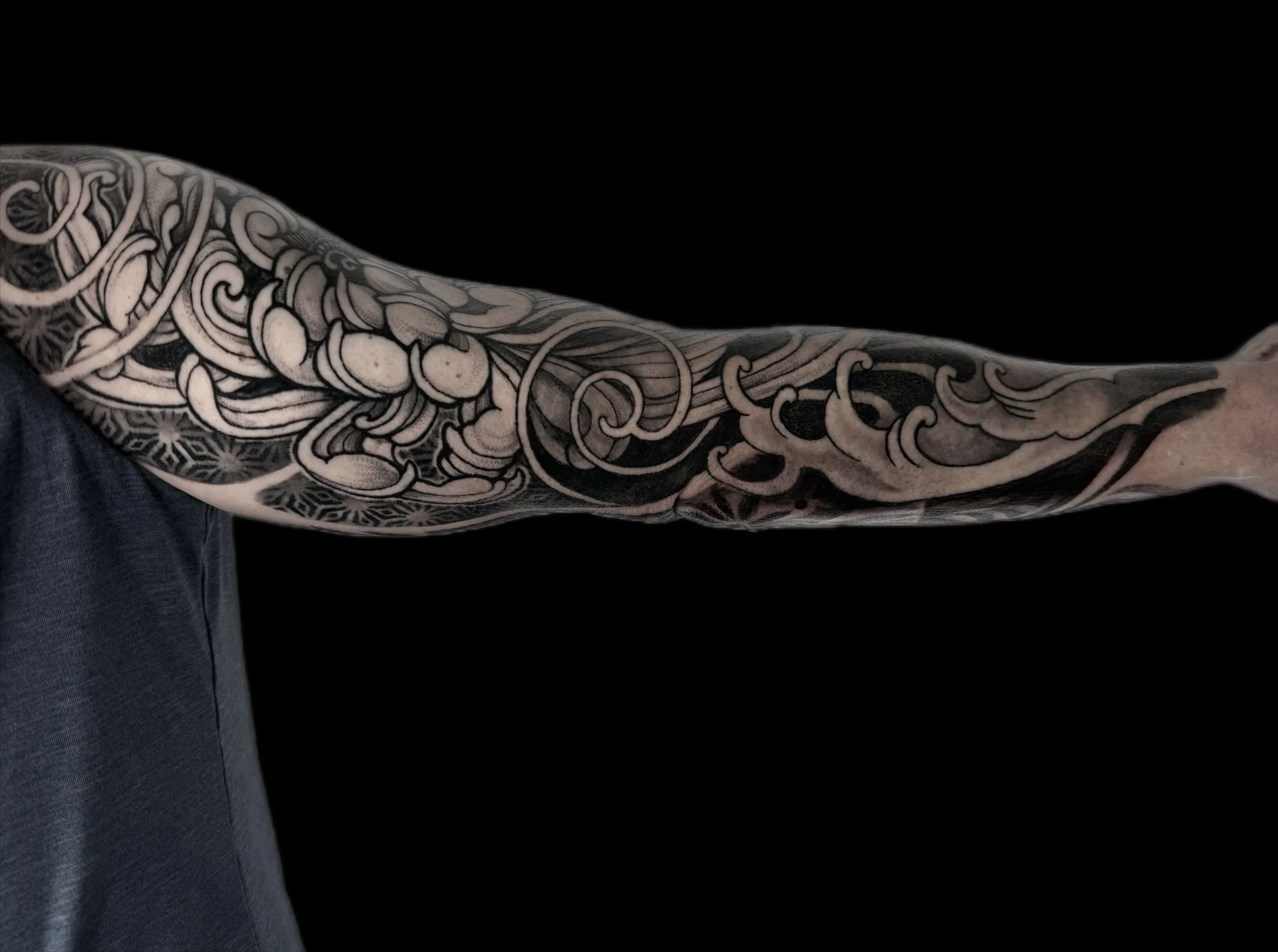 Close-up of a person's arm with a detailed black and white tattoo sleeve featuring abstract and floral designs.