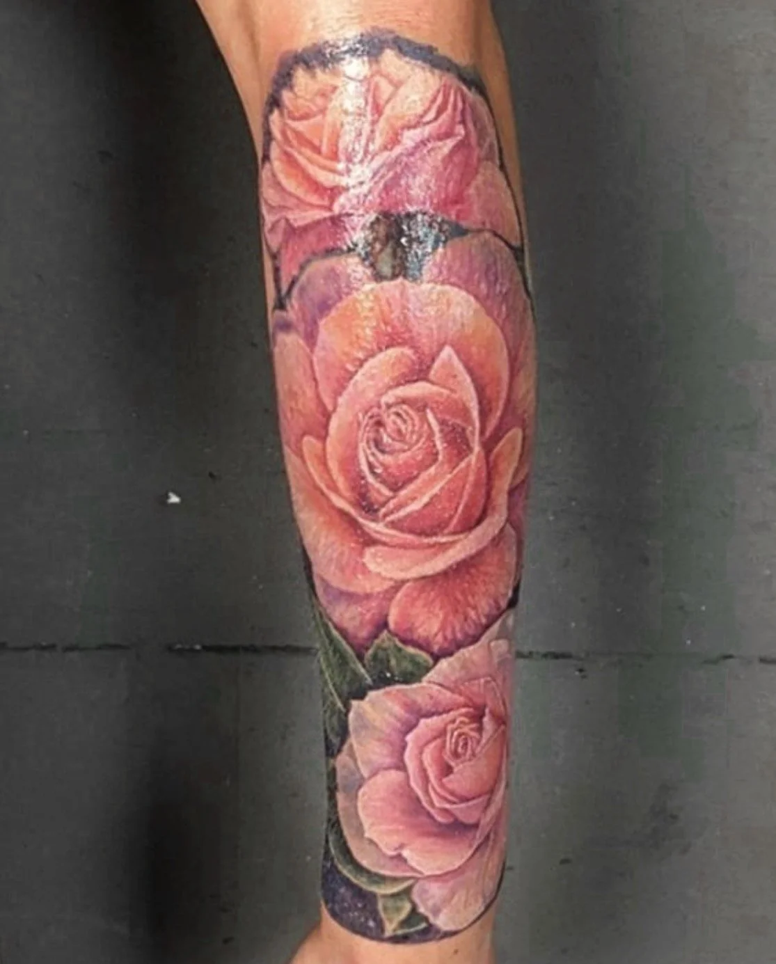 Colorful tattoo of large pink roses and a butterfly on a person's forearm.