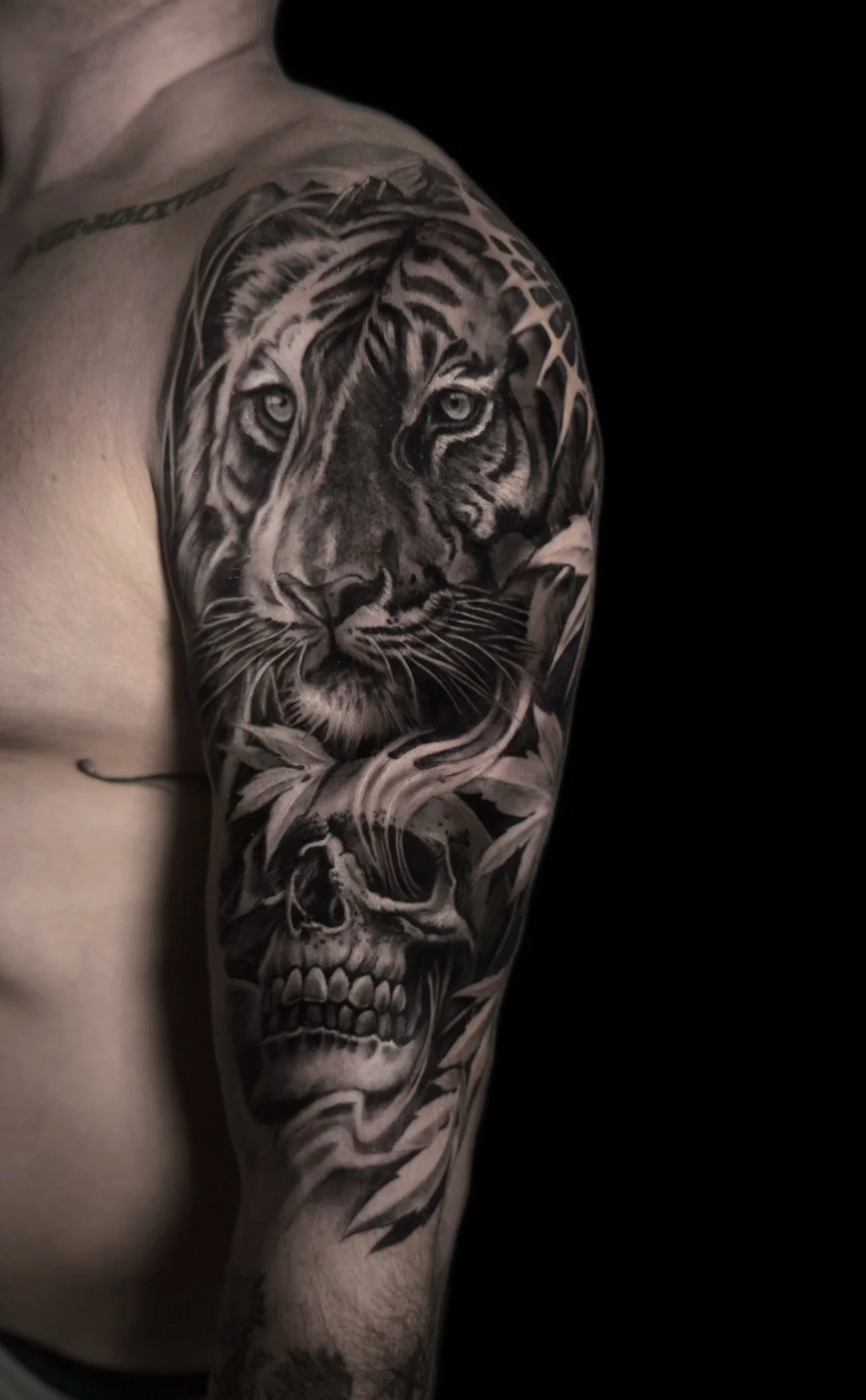 A tattoo of a tiger's face on a person's upper arm, blending into a skull with flowers on a dark background.
