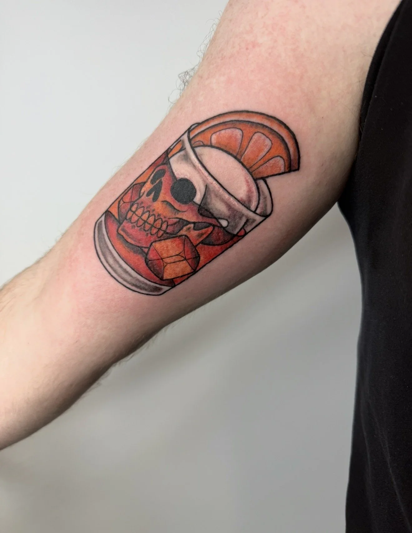 Tattoo of a skull with a glass of orange juice and an orange slice on the arm.