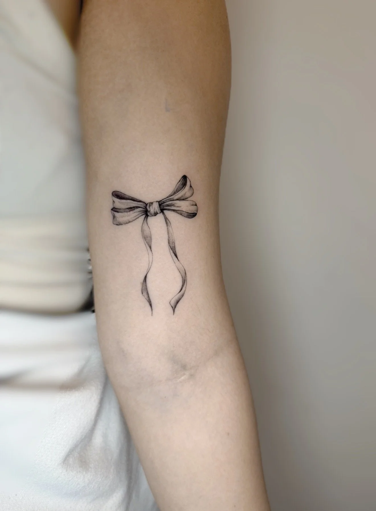 Fine line ribbon bow tattoo on inner arm