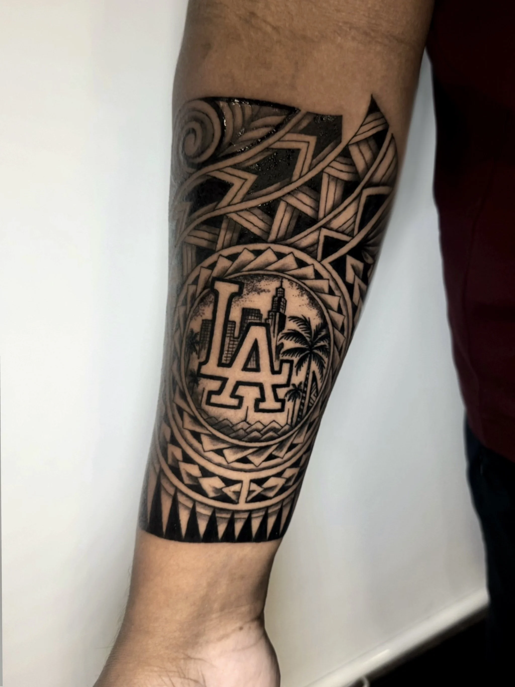 Tattoo sleeve on person's arm featuring geometric patterns, cityscape with skyscrapers, and a stylized depiction of the LA skyline with palm trees.