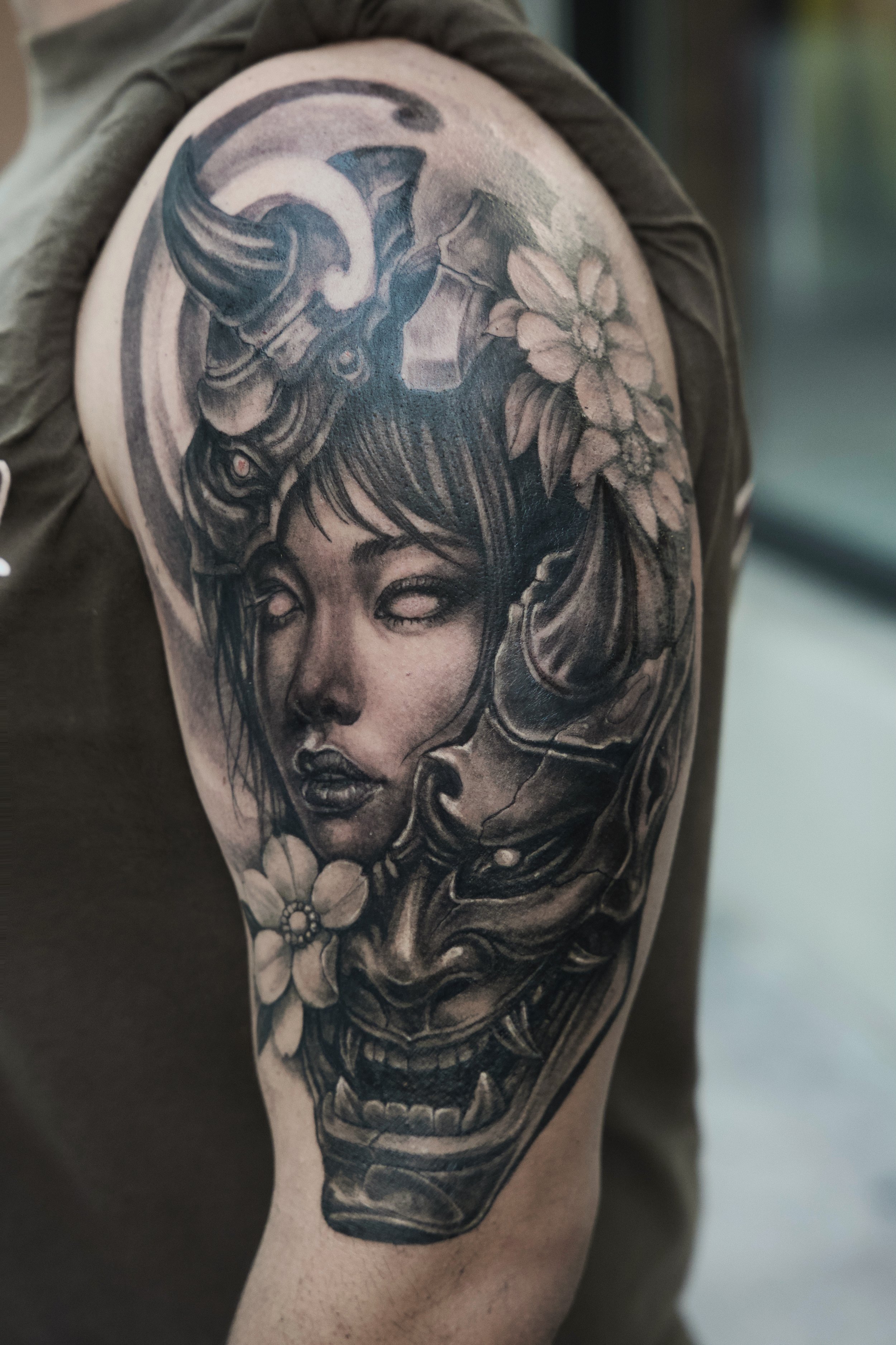 Black and gray tattoo of a woman's face with flowers and a dragon on the shoulder.