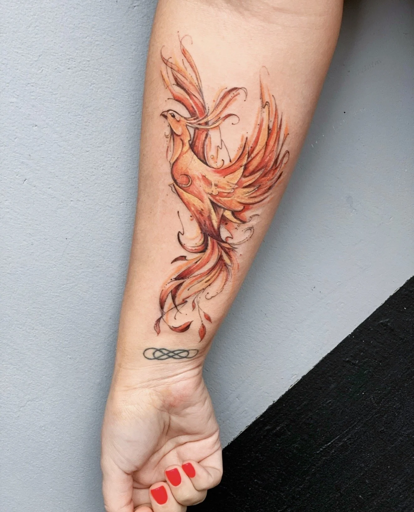 Watercolor-style tattoo of a phoenix on a person's forearm.